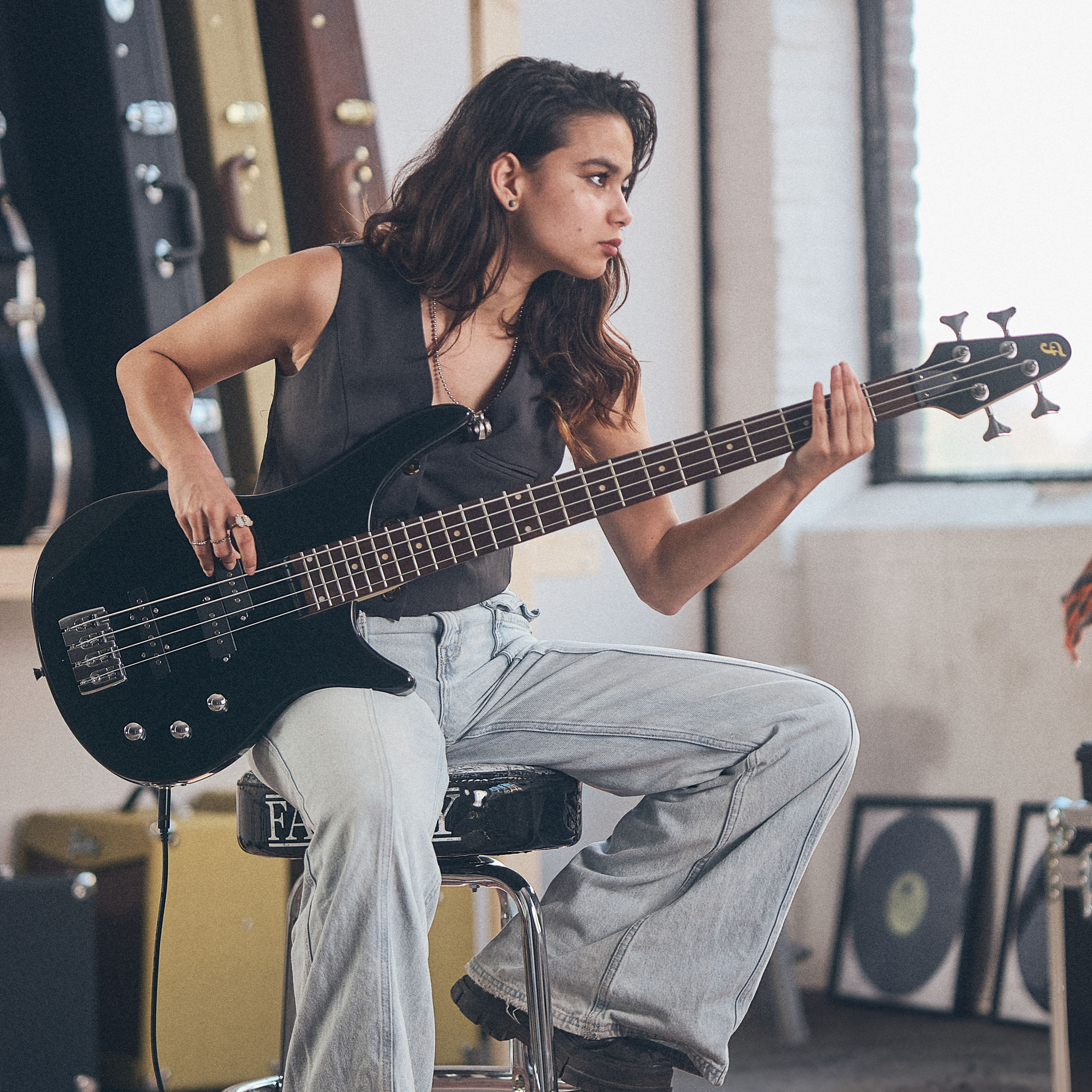 Een vrouw speelt basgitaar in een kamer met gitaarkoffers.