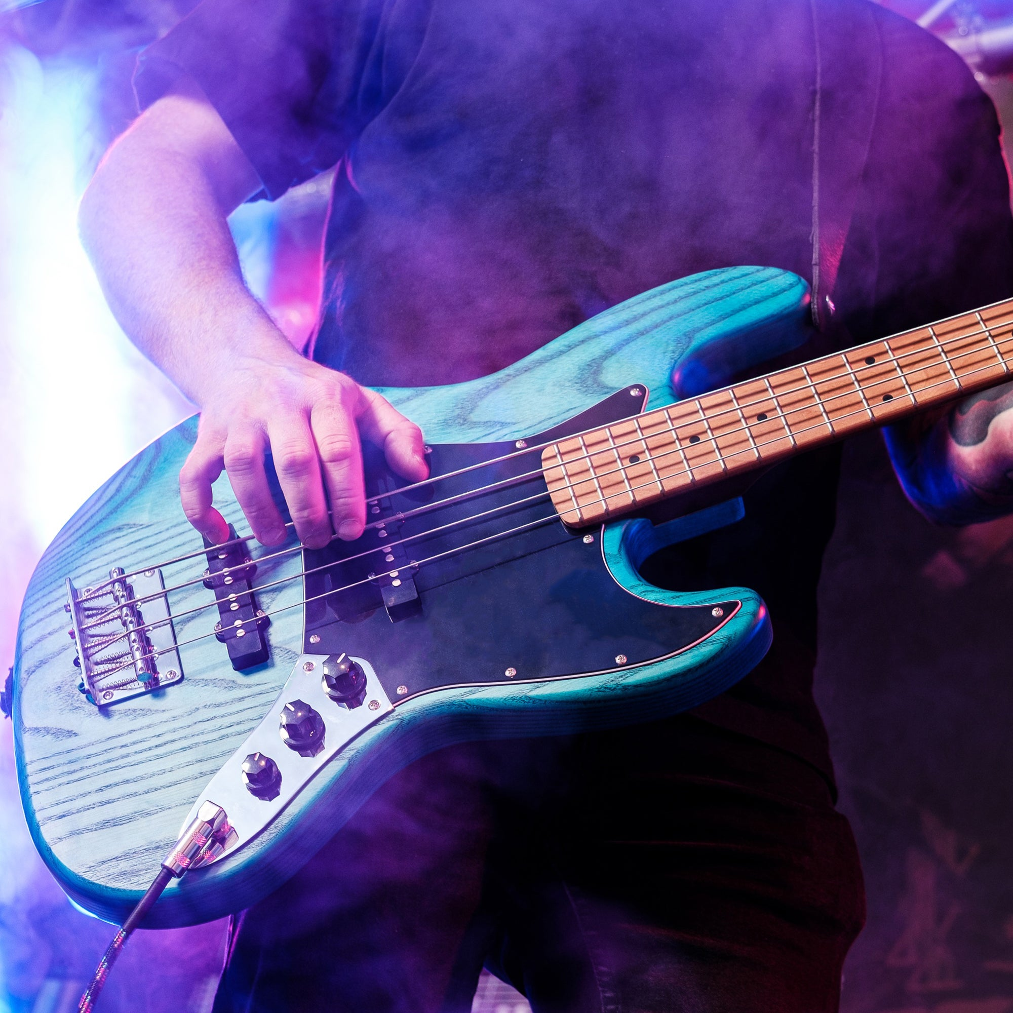 Een bassist bespeelt een blauw getinte basgitaar, verlicht door podiumlicht.