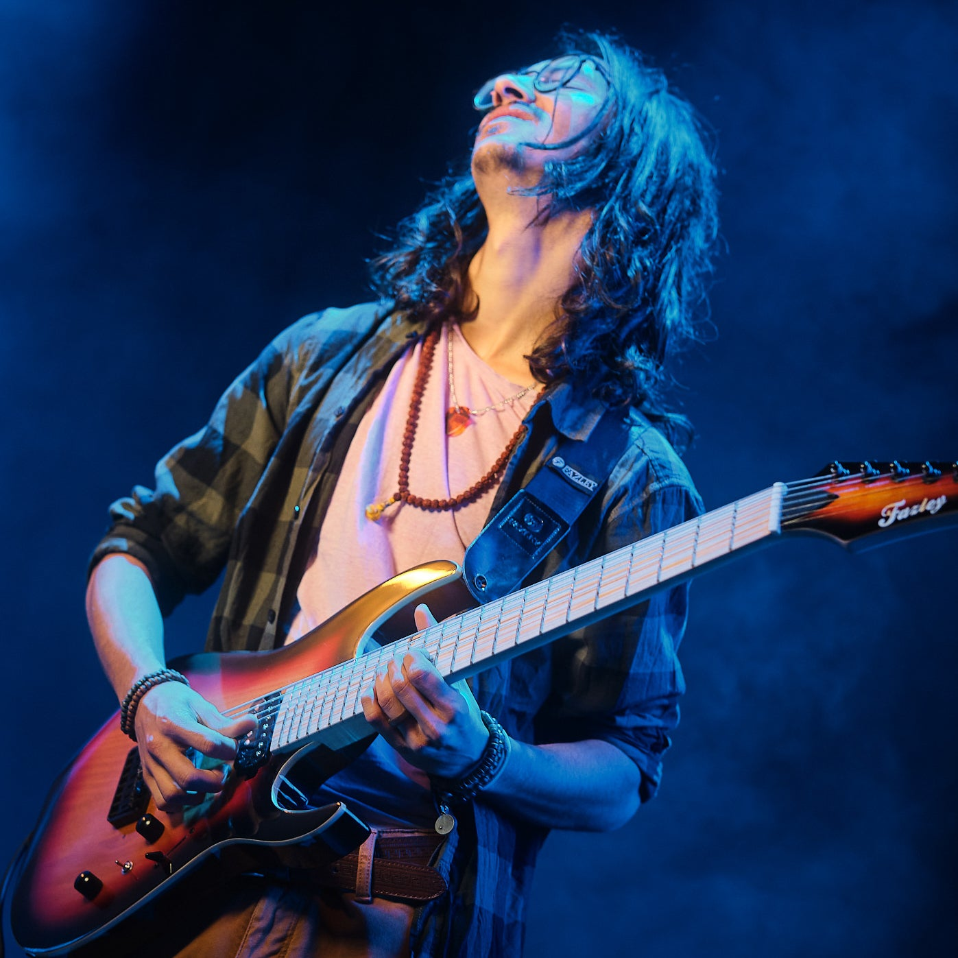 Een man met lang haar speelt gitaar op een podium in blauw licht.