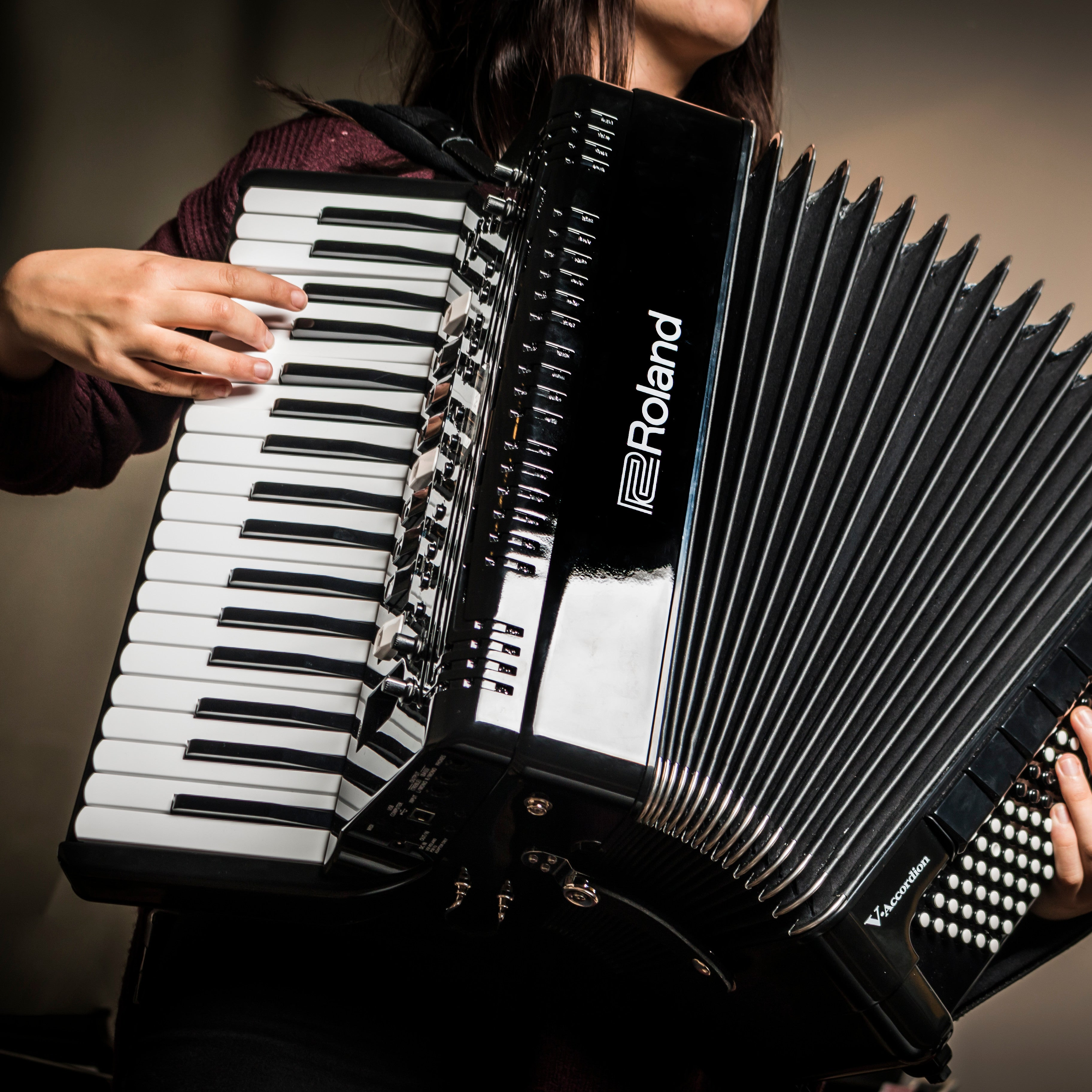 Een persoon bespeelt een zwarte Roland accordeon met witte pianotoetsen.