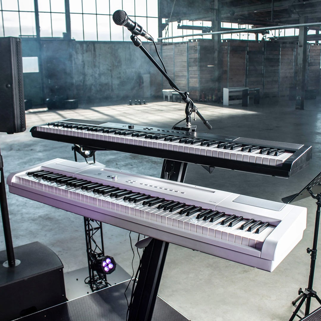 Twee keyboards op standaards, microfoon, luidspreker en lampen in industrieel gebouw.