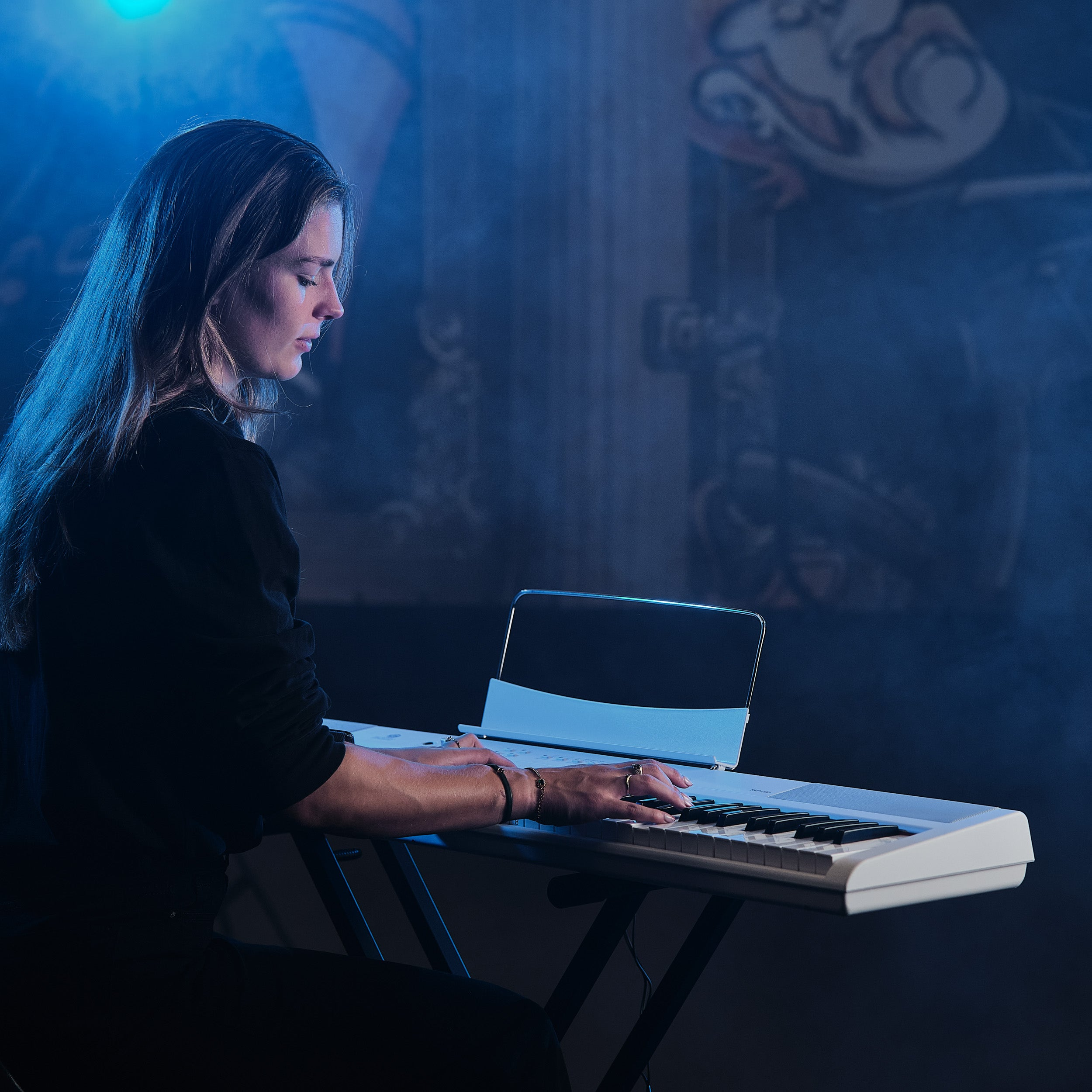 Een vrouw speelt op een wit keyboard, verlicht door blauw licht.