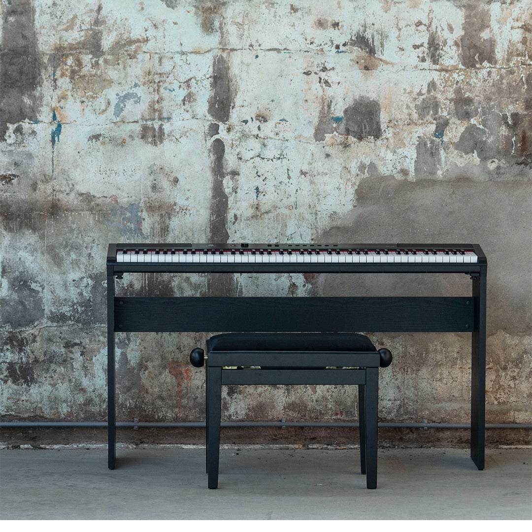Een zwart digitale piano met kruk voor een gestructureerde muur.