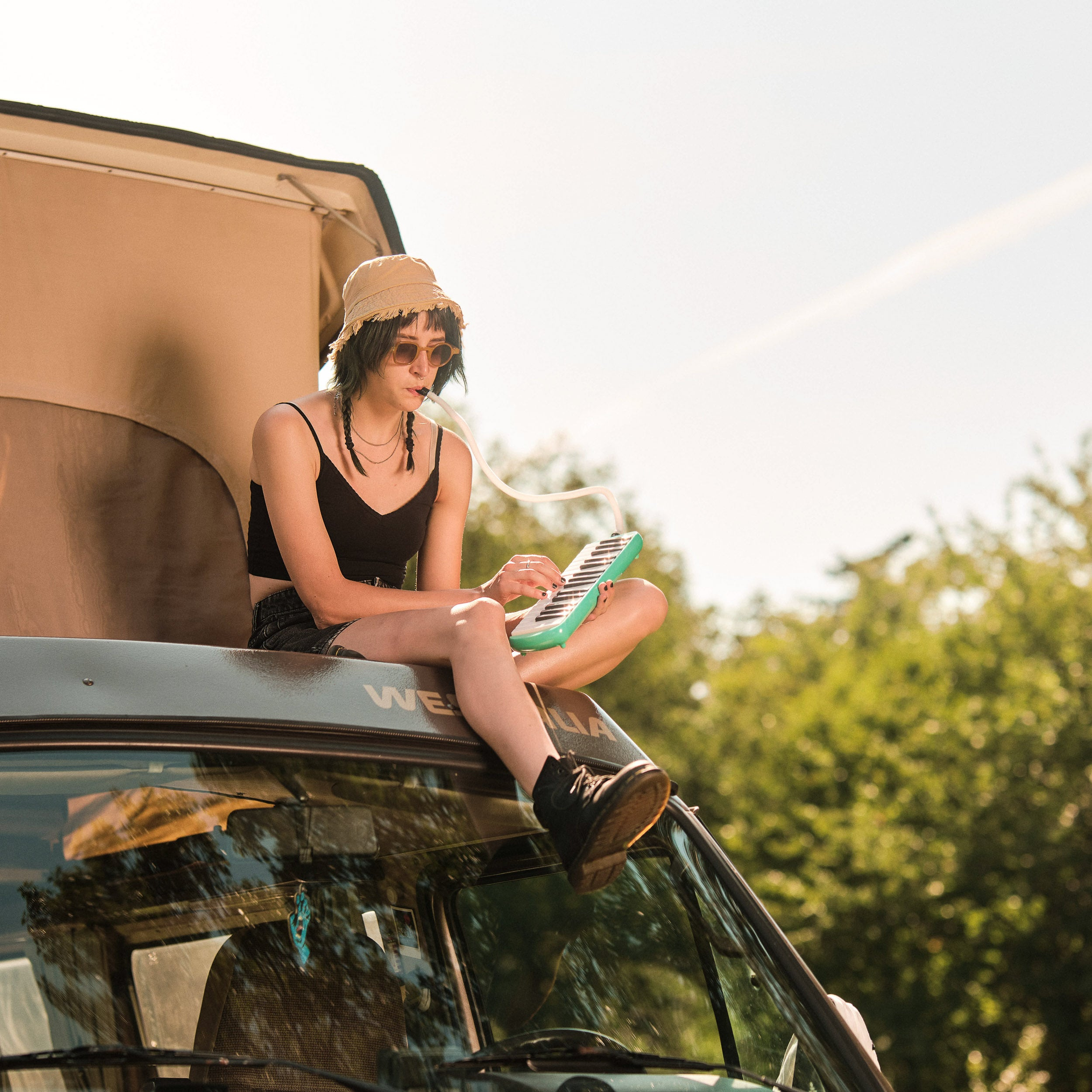 Jonge vrouw speelt melodica, zittend op een camper.