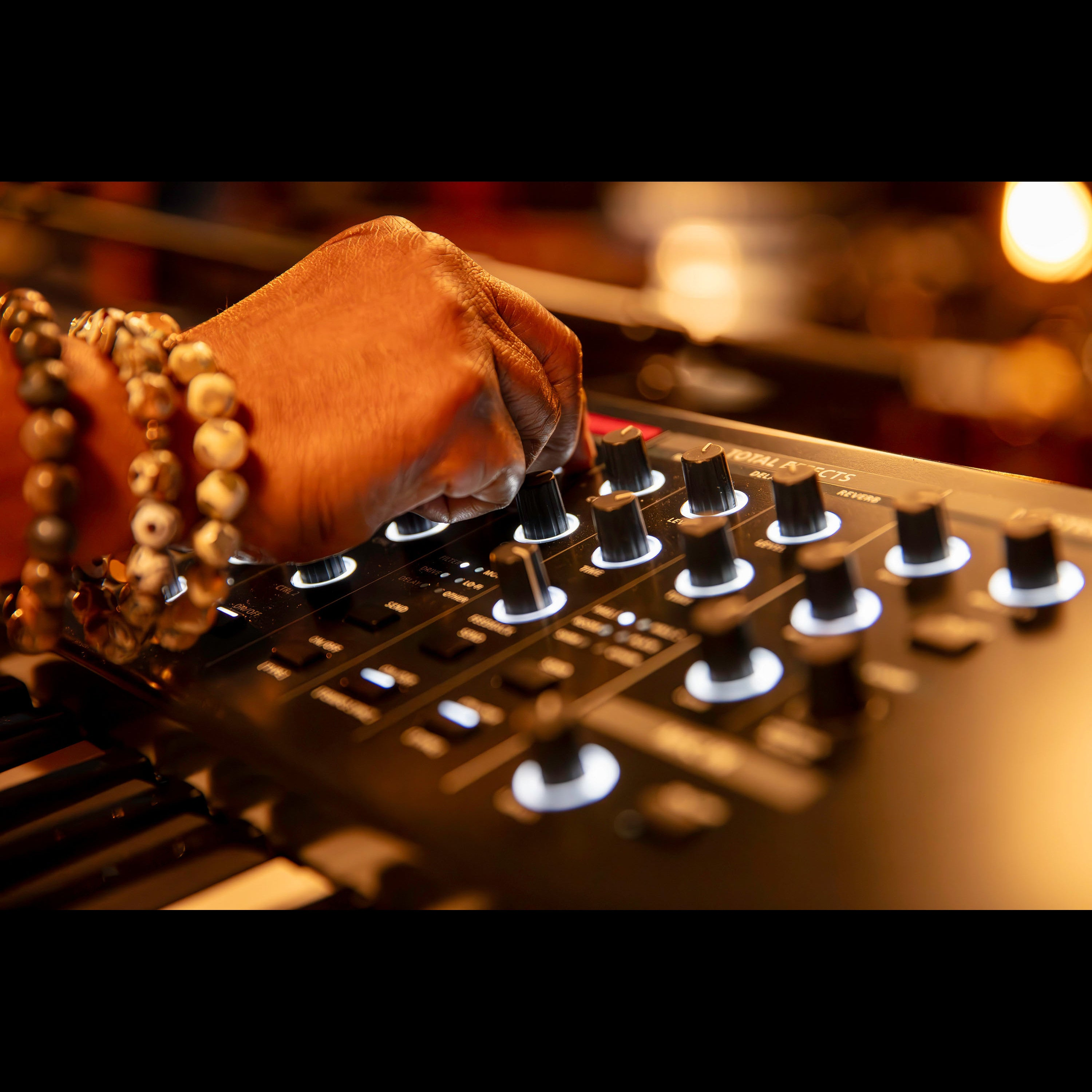 Een hand met armbanden draait aan een knop op een synthesizer.
