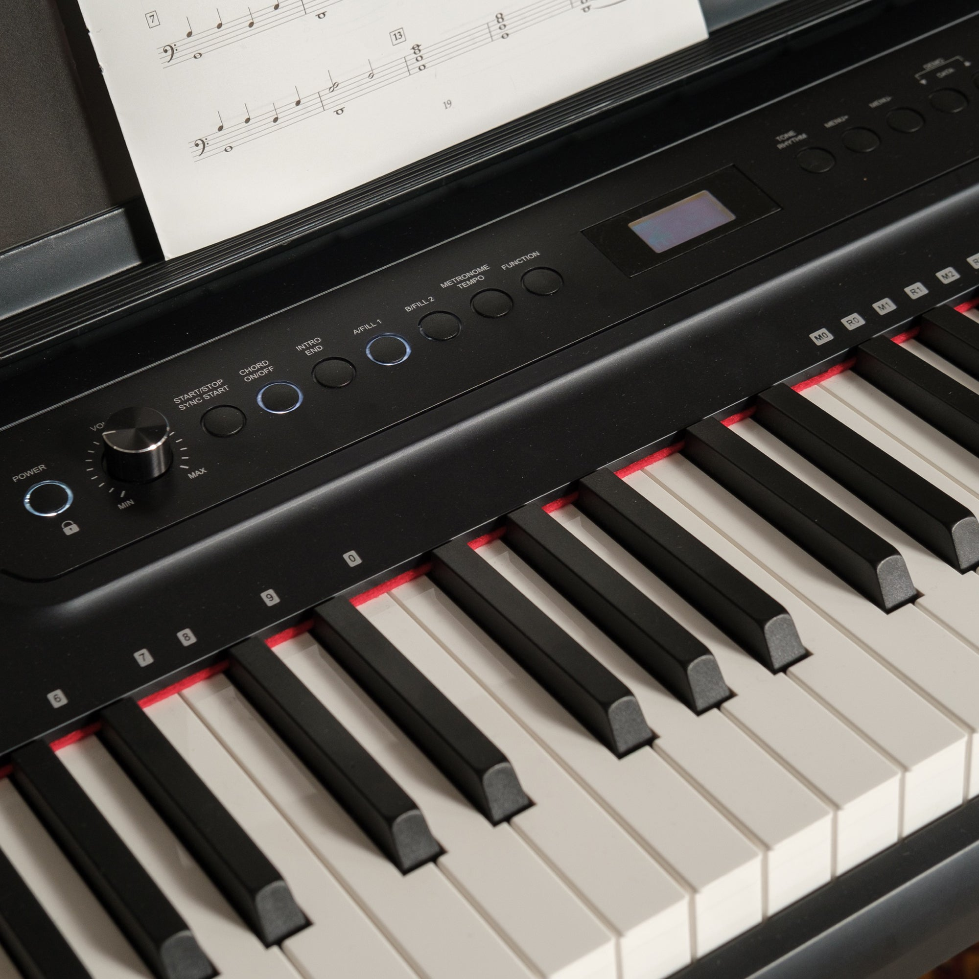 Een zwarte digitale piano met bladmuziek op de standaard en veel knoppen.