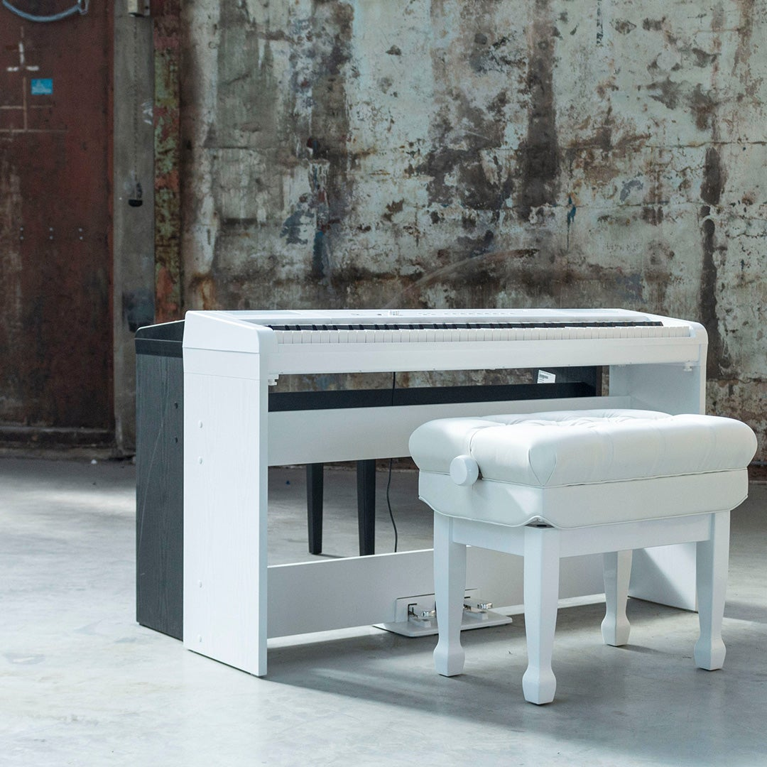 A white digital piano with a stool sits in front of a rustic wall.