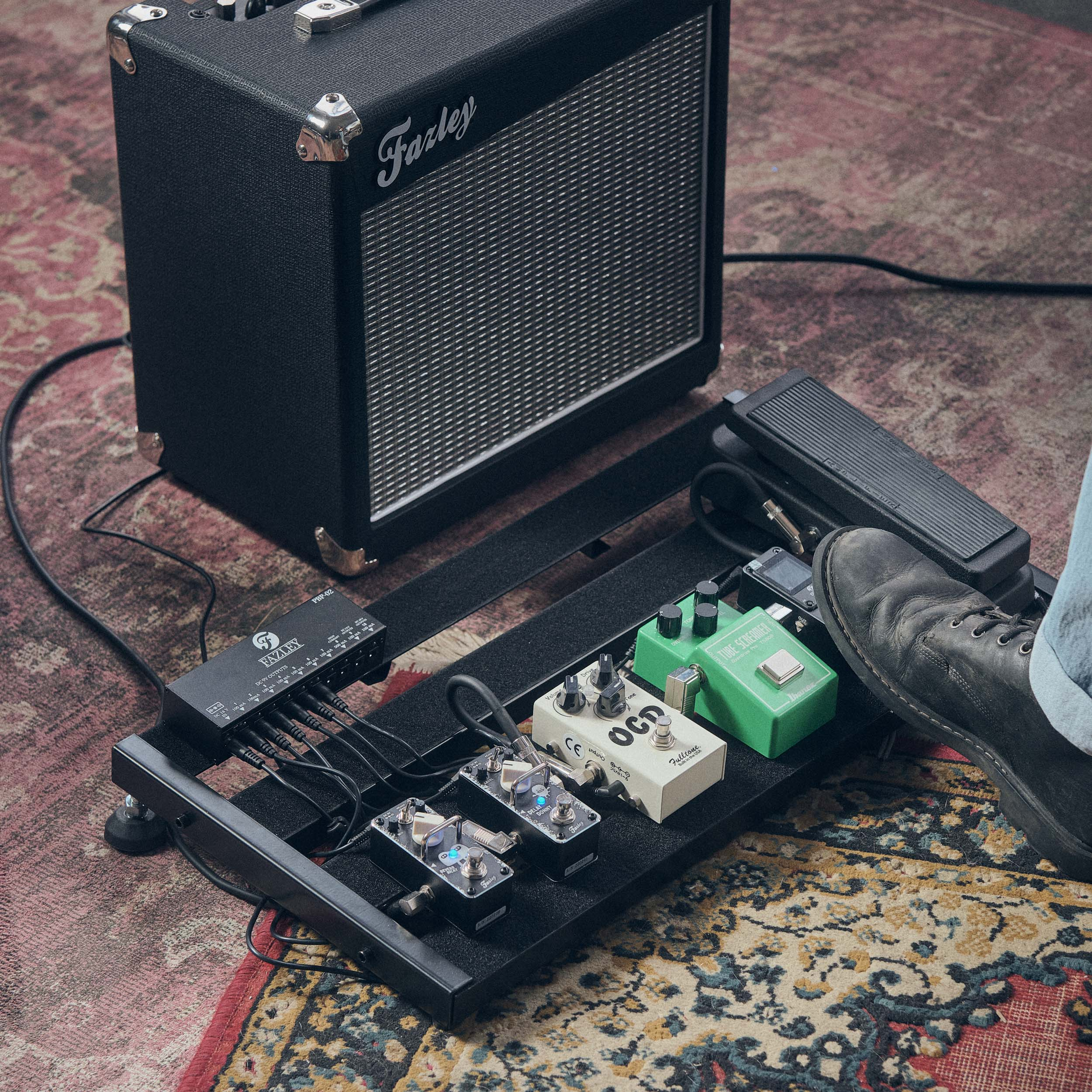 Een gitaarversterker naast een pedalboard met meerdere effectpedalen.