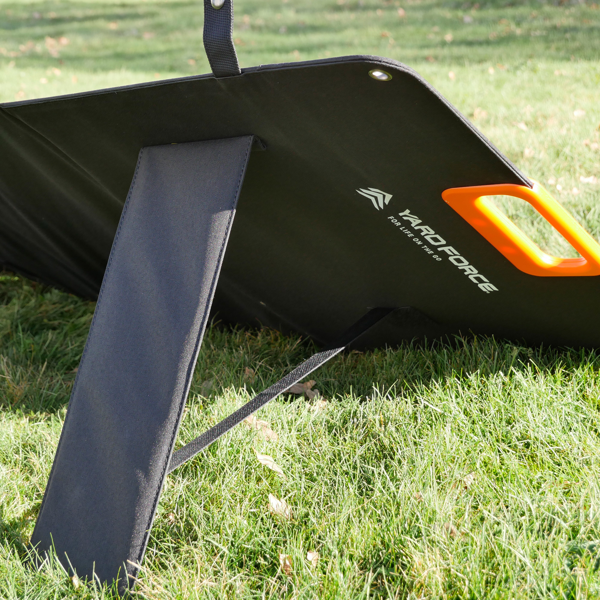 Schwarzes Solarpanel mit orangefarbenem Griff auf Gras.