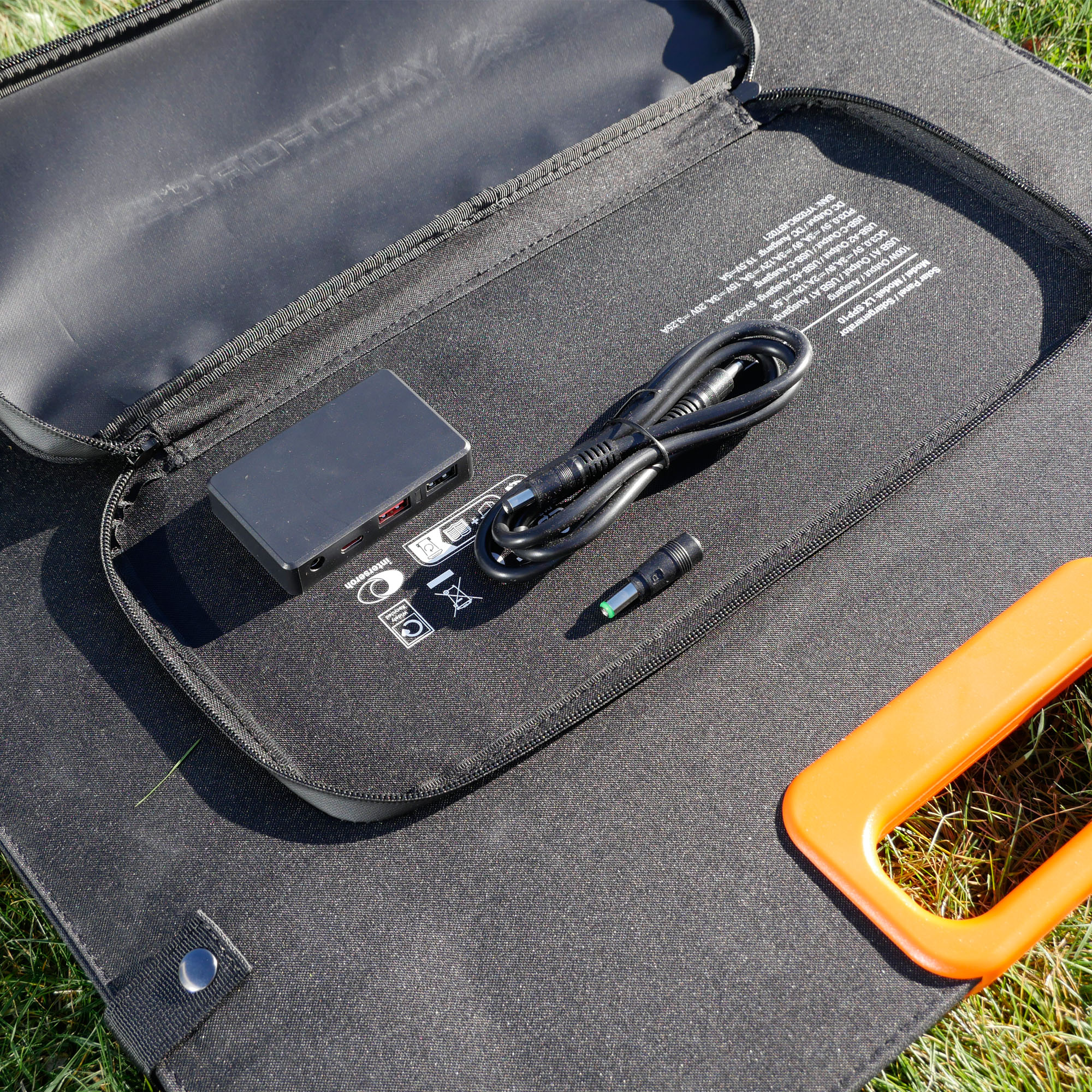 Schwarze Tasche mit Solarpanel-Zubehör: Adapter, Kabel und orangefarbener Griff.