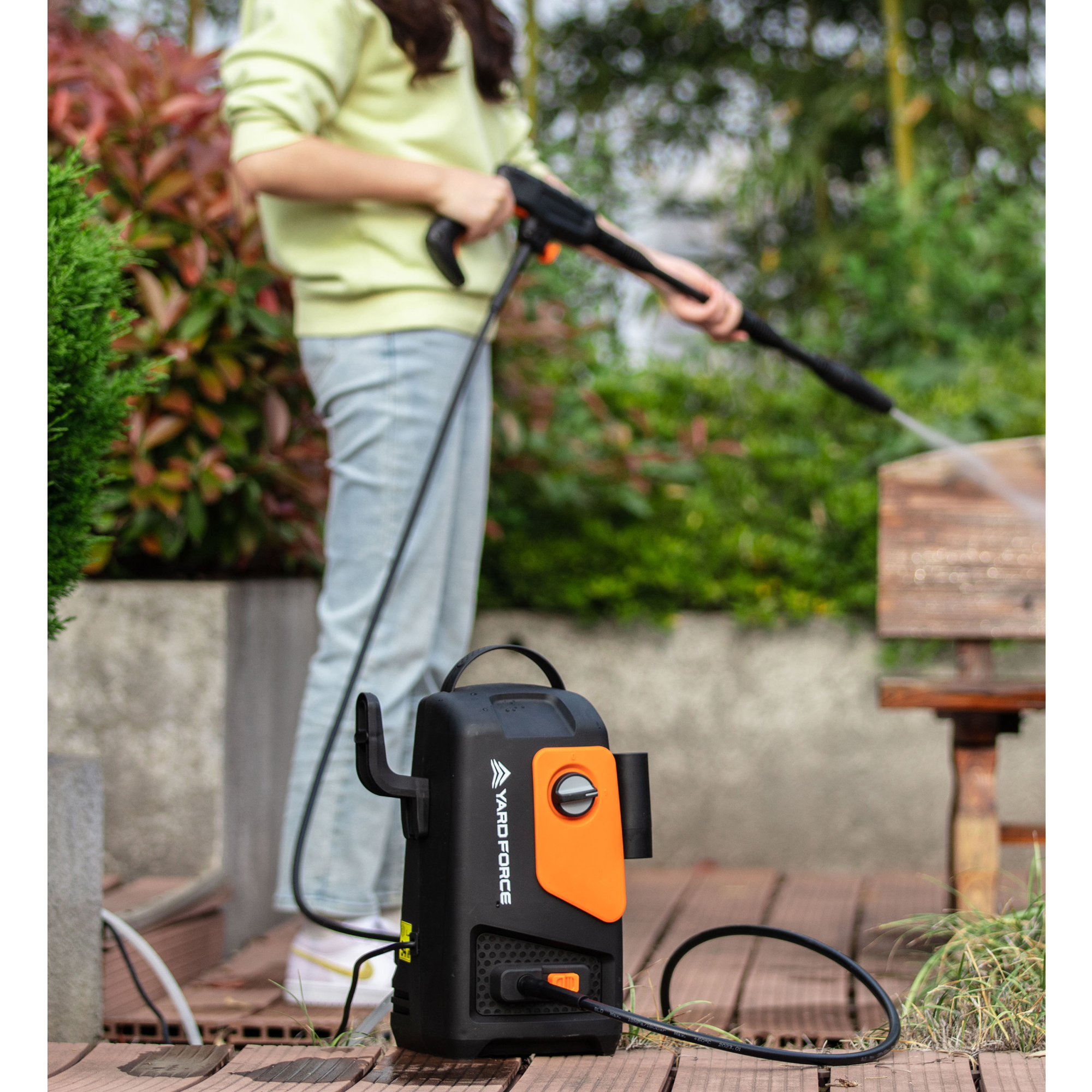 Eine Person reinigt Holz mit einem Hochdruckreiniger in einem Garten.