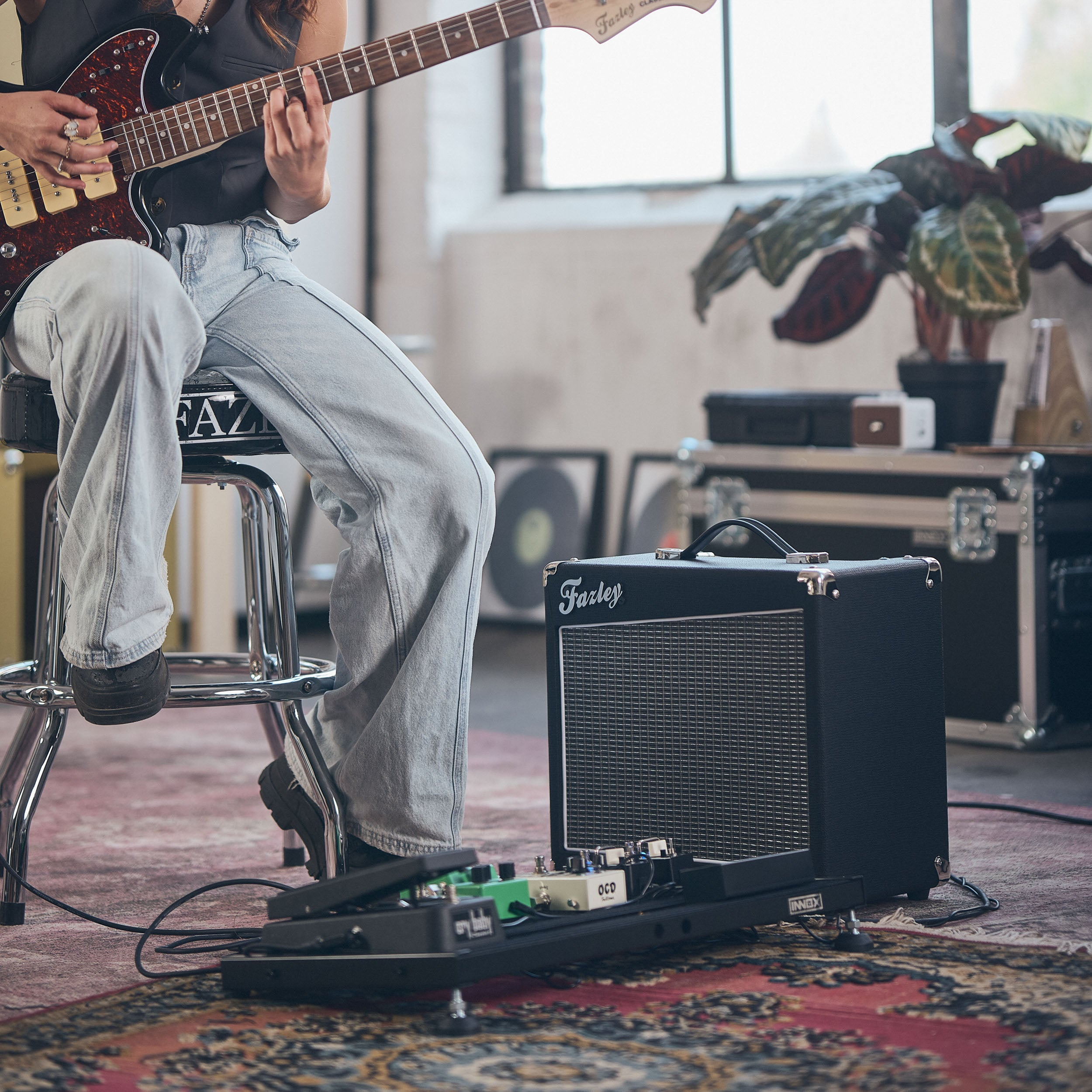 Persoon speelt gitaar naast versterker en pedalboard op een vloerkleed.