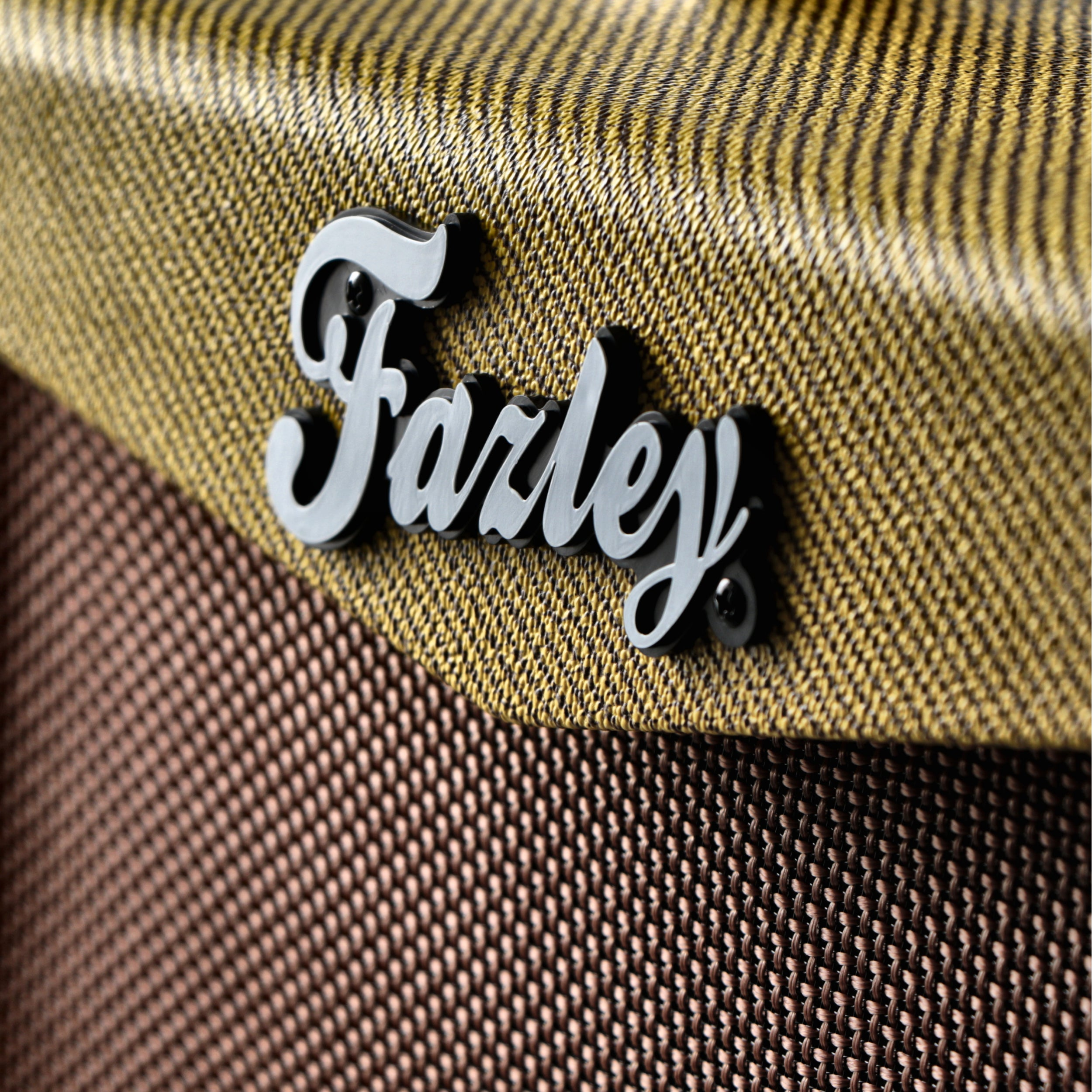 Close-up van een gouden luidsprekergrille met de gestileerde zwarte tekst "Farley".