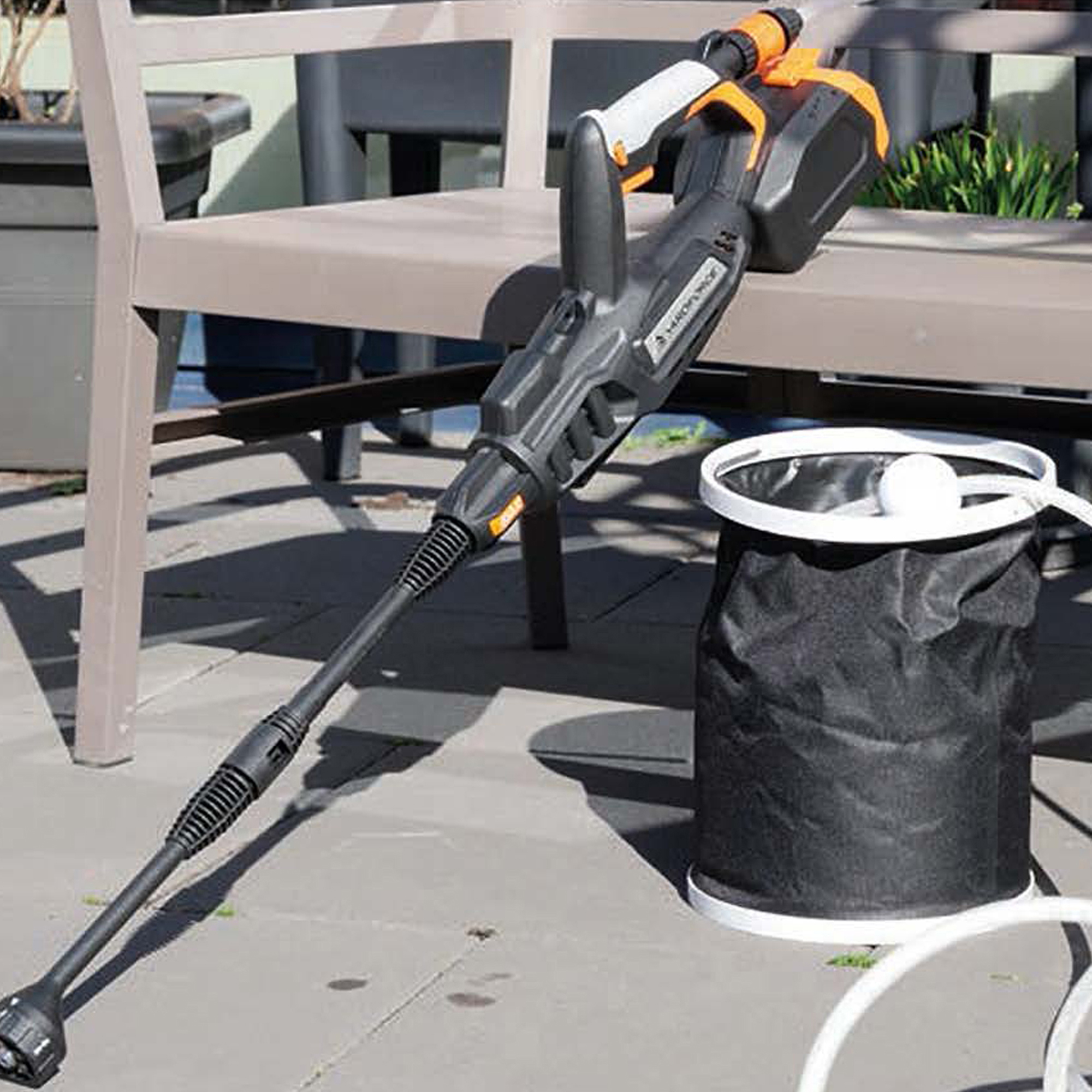 Ein tragbares Hochdruckreiniger-Set mit Schlauch und Eimer liegt auf einer Terrasse.
