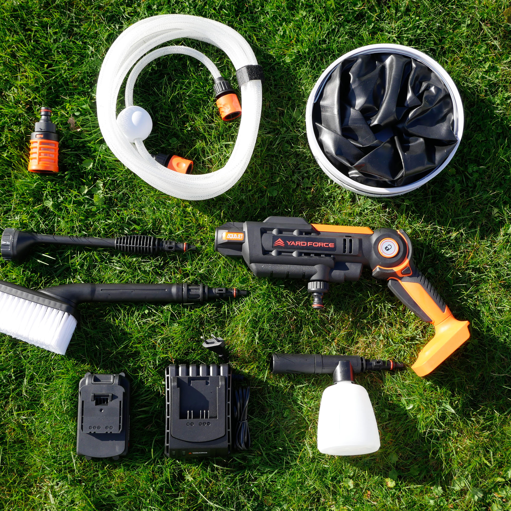 Ein Hochdruckreiniger-Set mit Schlauch, Bürsten, Akkus und Ladegerät auf Gras.