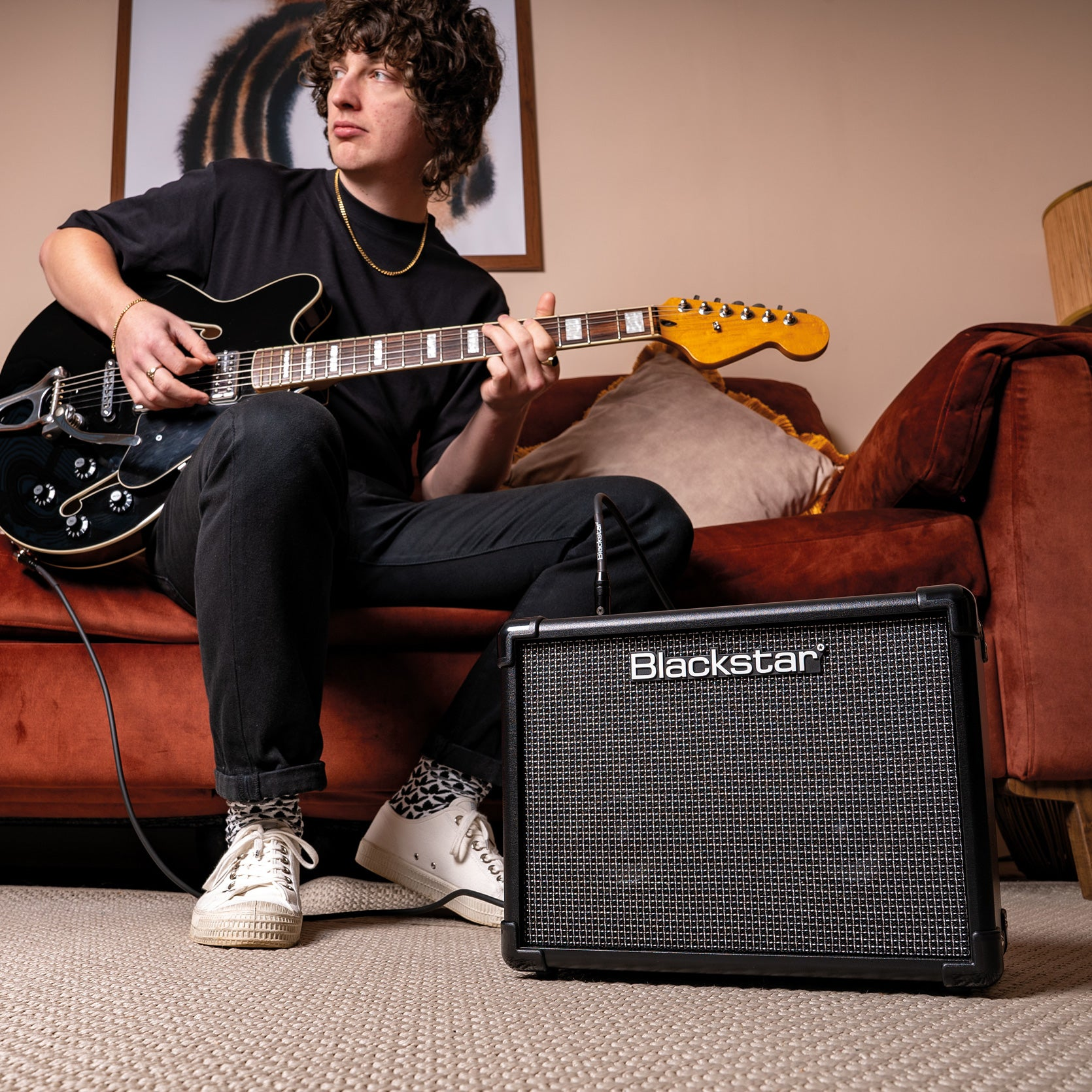 Een man met krullend haar speelt op een zwarte elektrische gitaar naast een Blackstar versterker.
