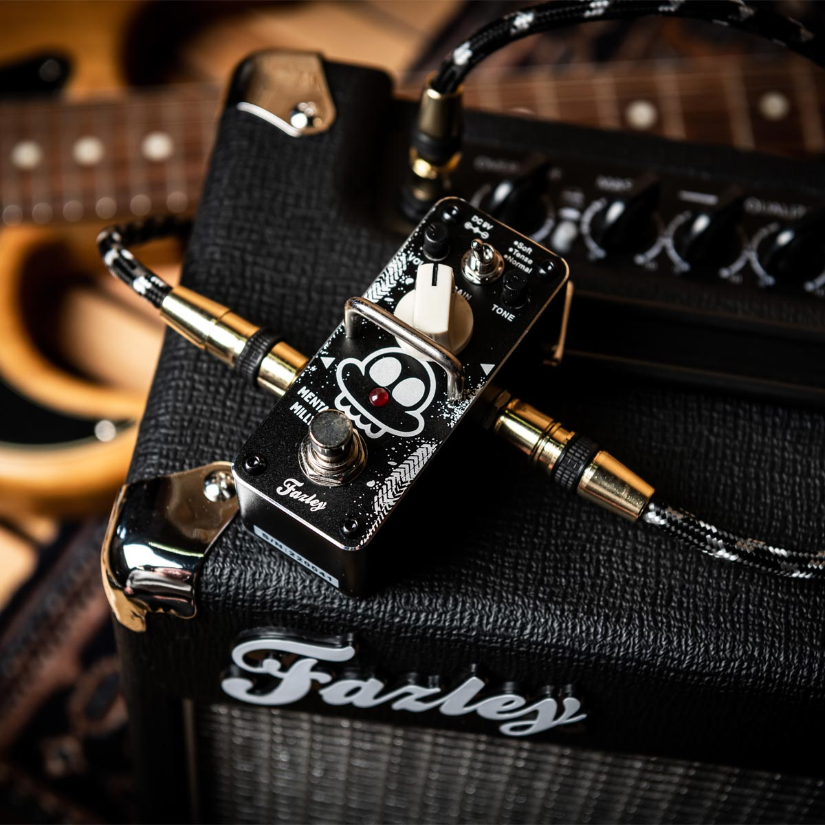 A guitar amplifier with a pedal and guitars in the background.