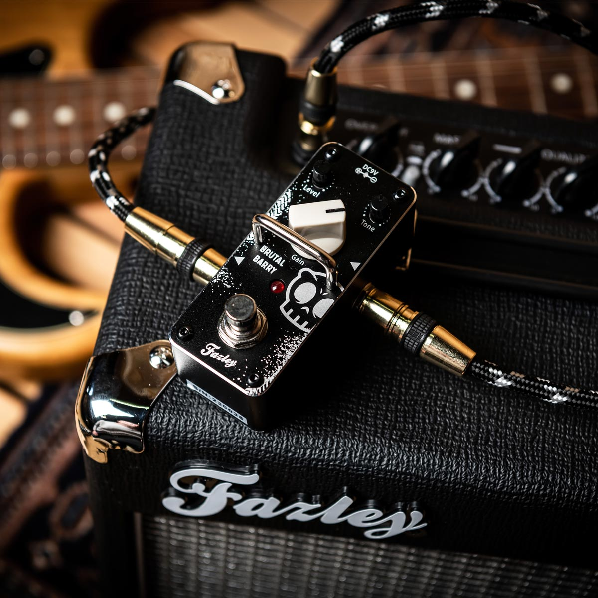 A black guitar amp with an effect pedal and guitars in the background.