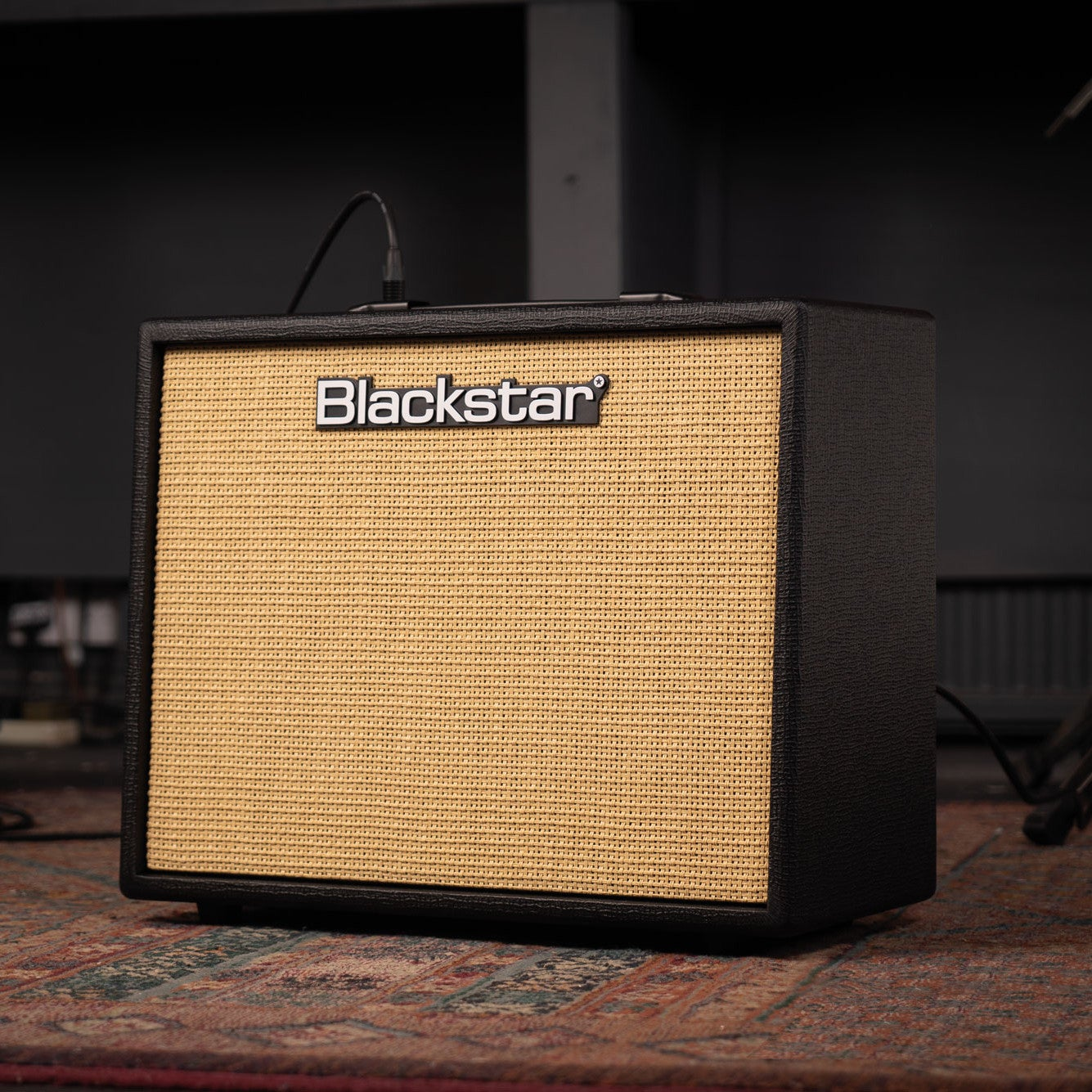 Een Blackstar gitaarversterker met een lichtbruin speakerrooster staat op een vloerkleed.
