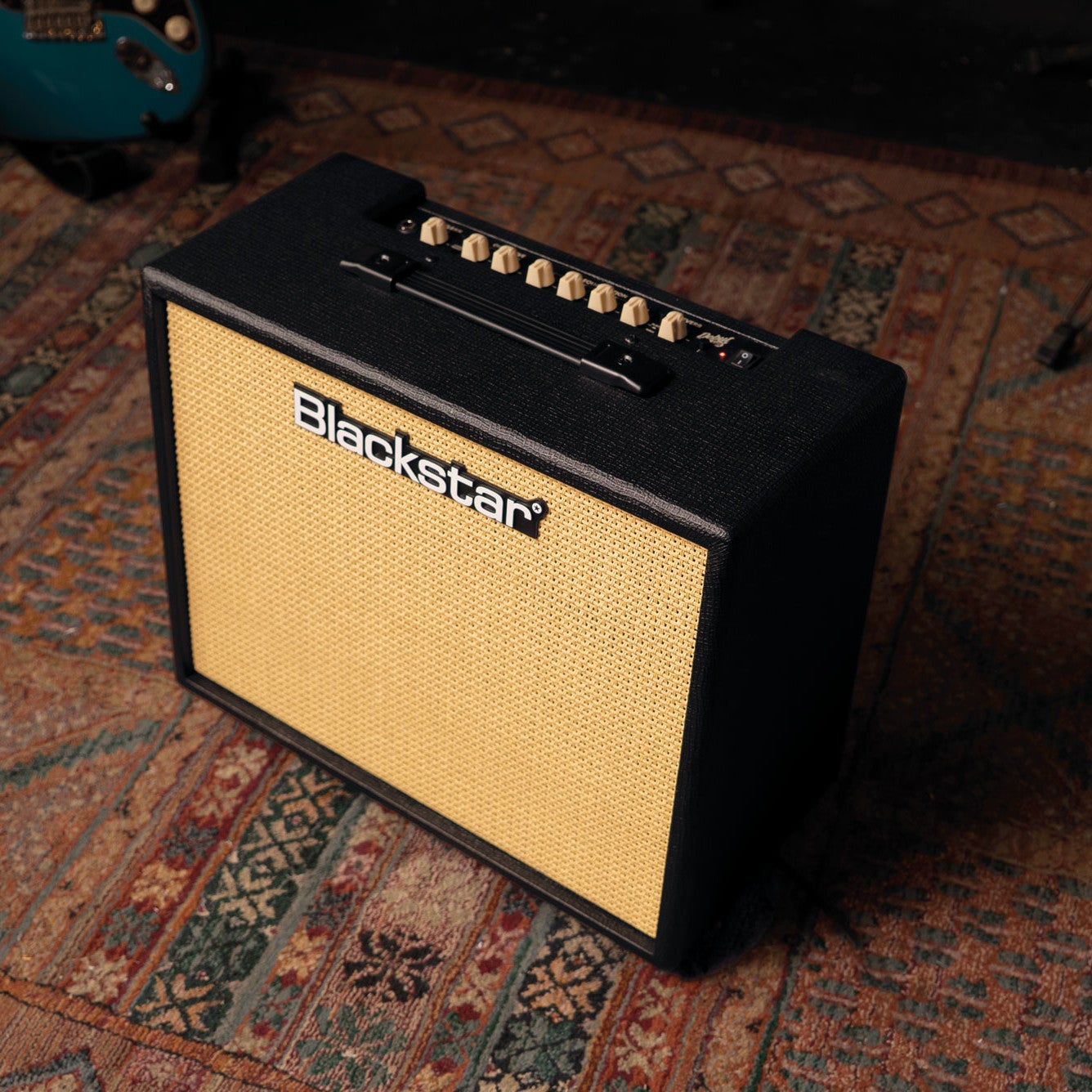 Een zwarte Blackstar gitaarversterker met gele speakergrill staat op een kleed.