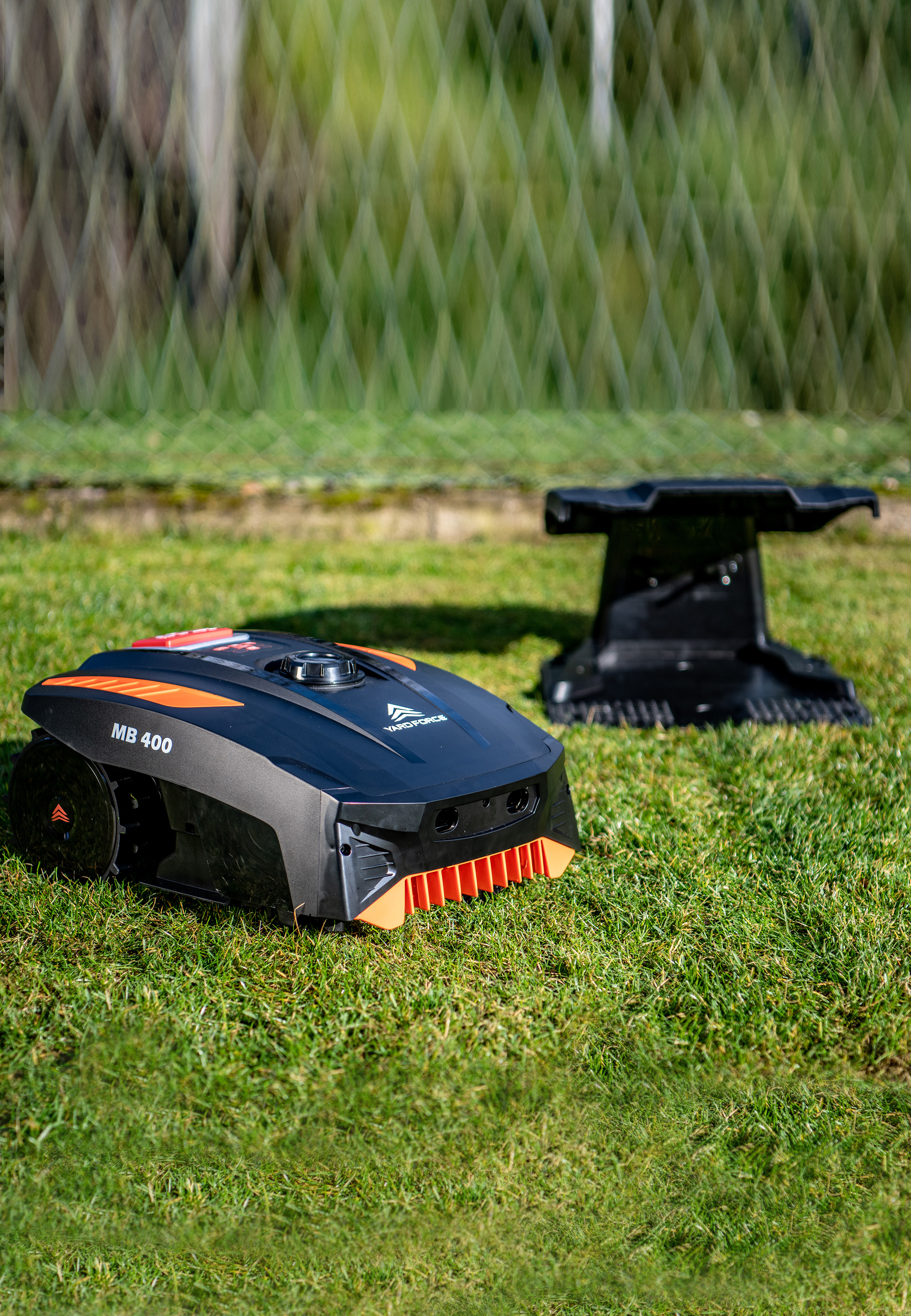 Ein schwarzer Rasenmähroboter mit orangen Akzenten steht auf Gras.