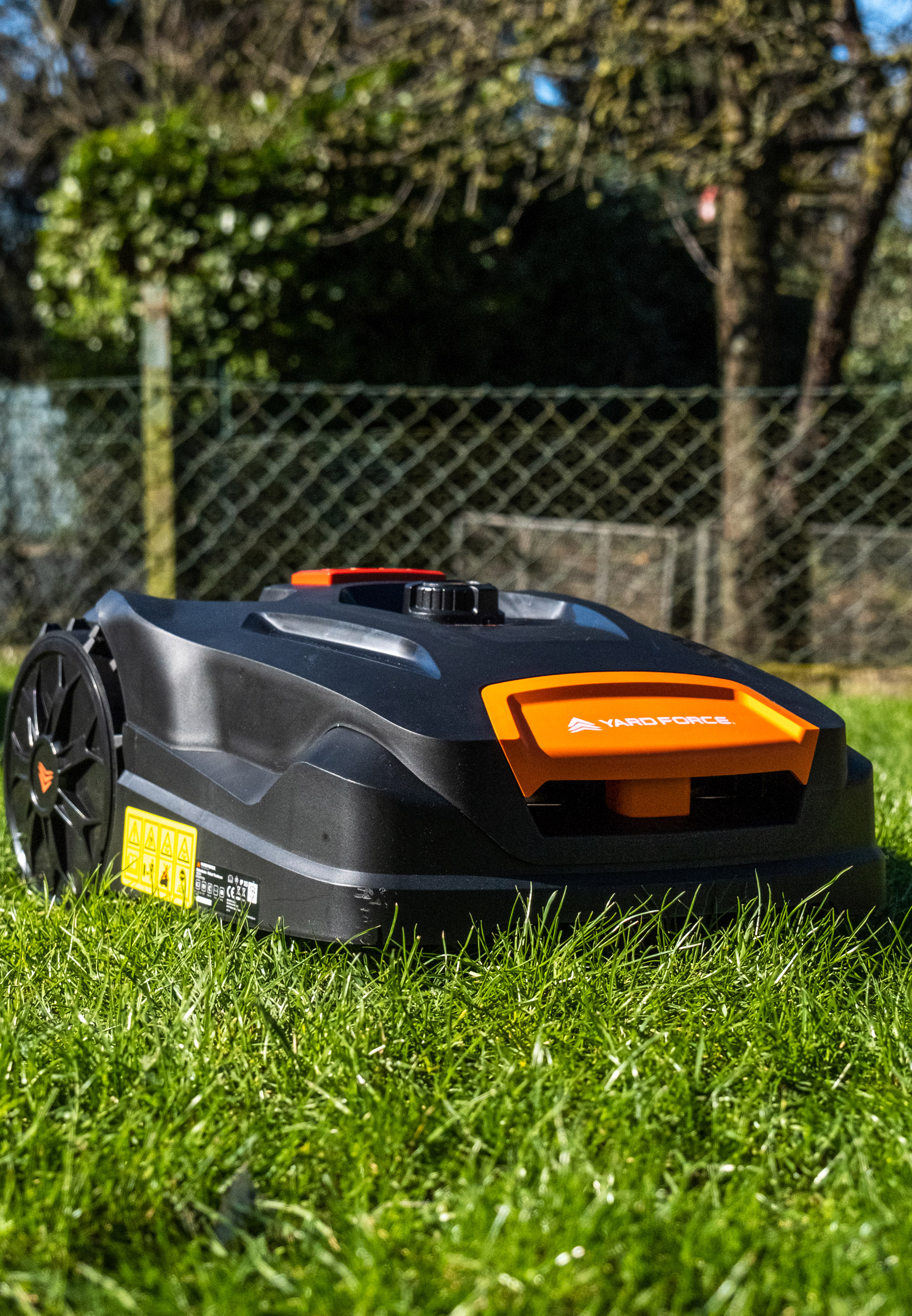 Ein schwarzer Rasenmähroboter mit orangefarbenen Akzenten steht auf grünem Gras.
