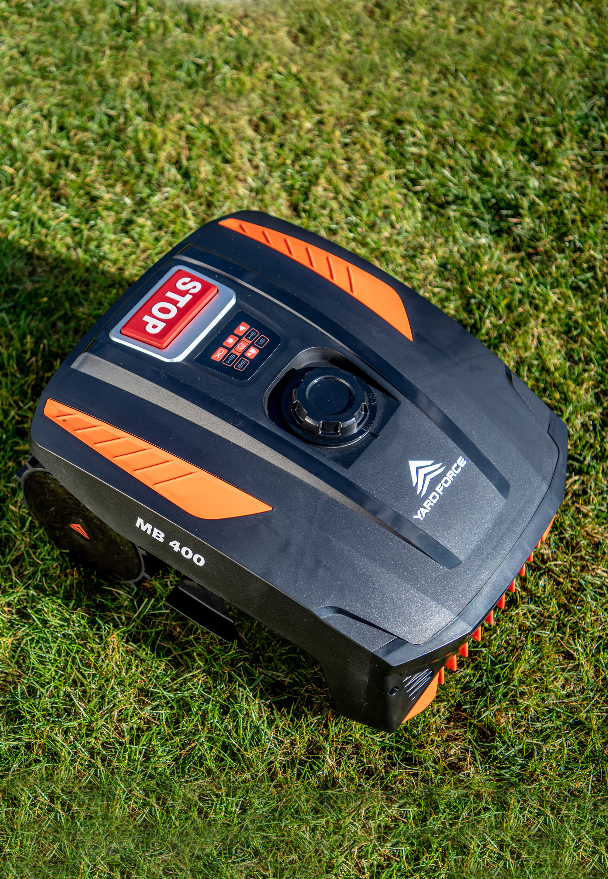 Ein schwarzer Rasenmähroboter mit orangefarbenen Akzenten steht auf grünem Gras.