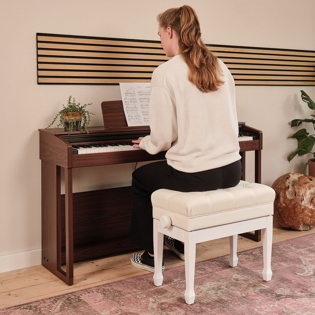 A woman plays piano on a brown piano, sitting on a white bench.