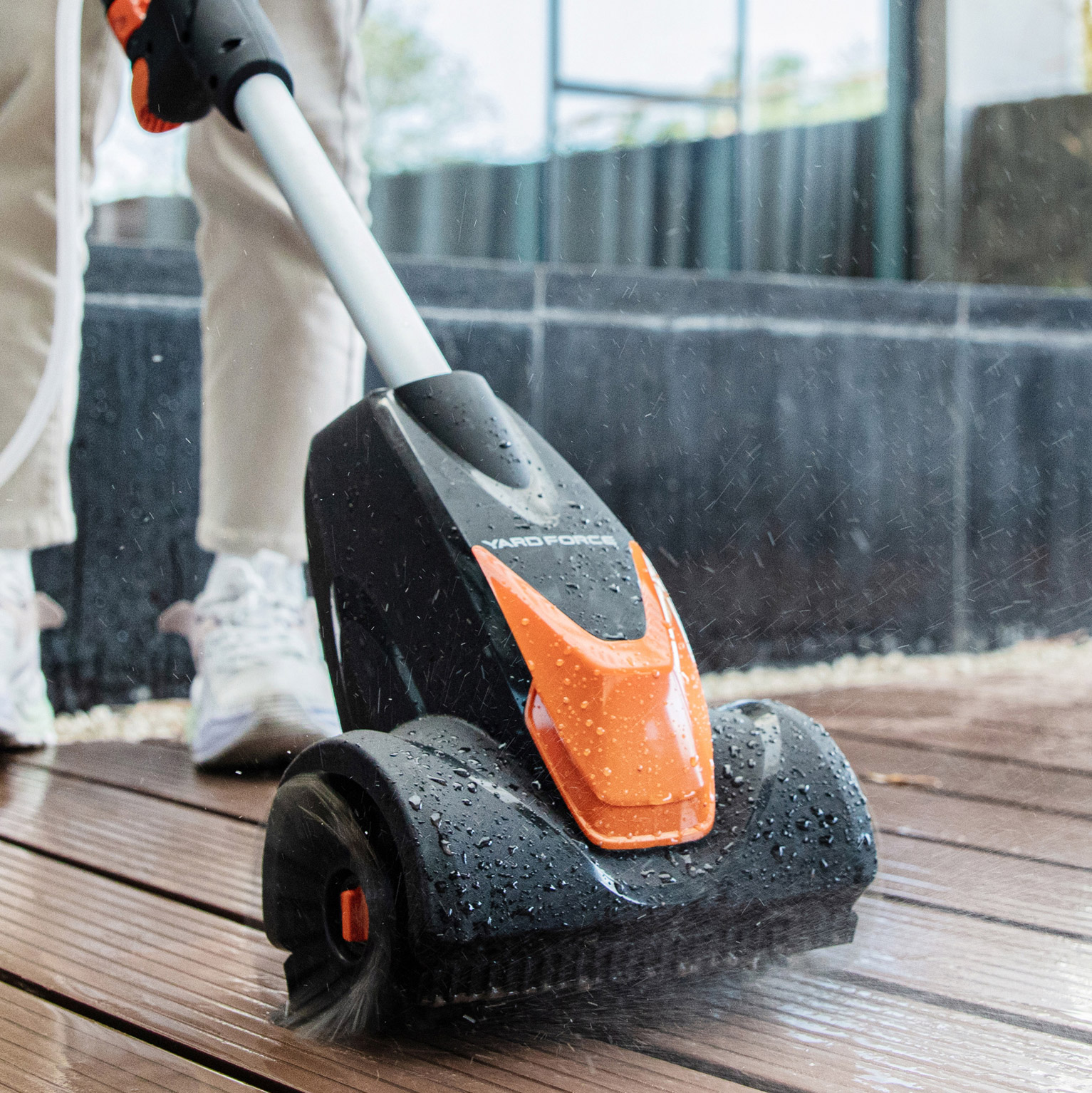 Ein orange-schwarzer Reiniger mit Bürsten reinigt eine Holzterrasse.