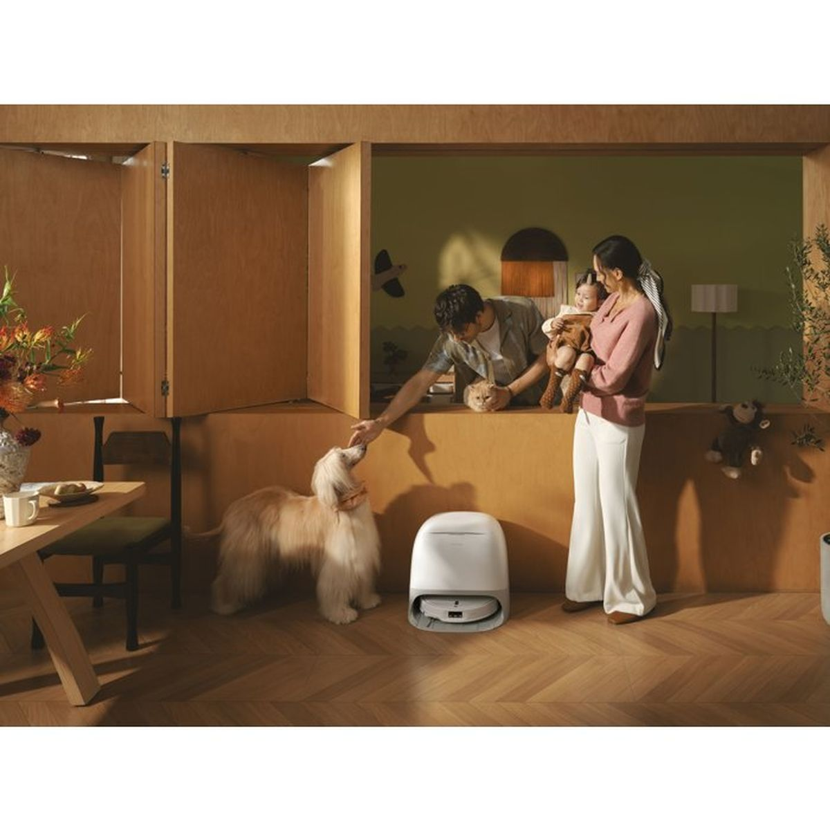 Uomo accarezza cane, donna tiene bimbo, gatto su bancone, aspirapolvere robot.