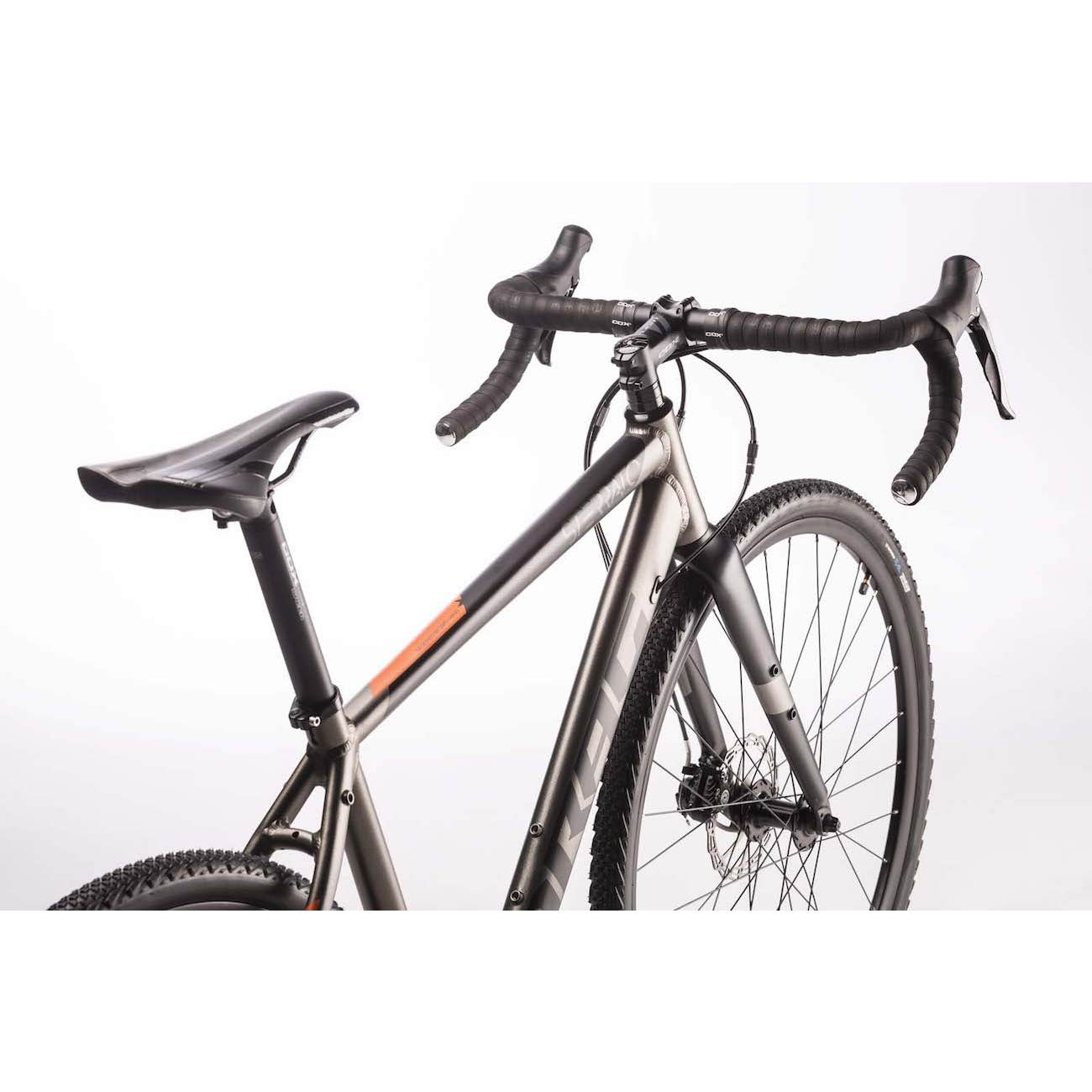 Ein graues Gravelbike mit schwarzen Lenkergriffen und Reifen. Ein orangefarbener Akzent.