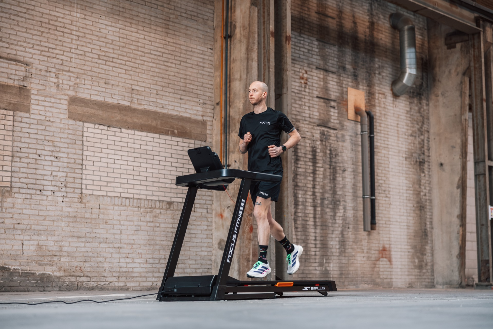 A man runs on a treadmill in an industrial hall against a brick wall.