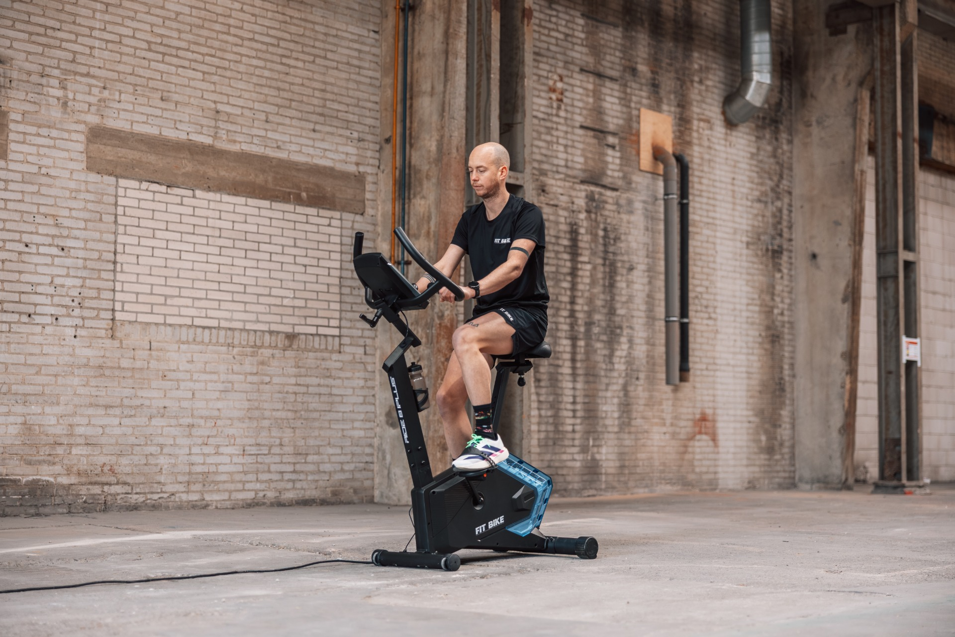 Een man op een hometrainer in een industriële hal met bakstenen muren.