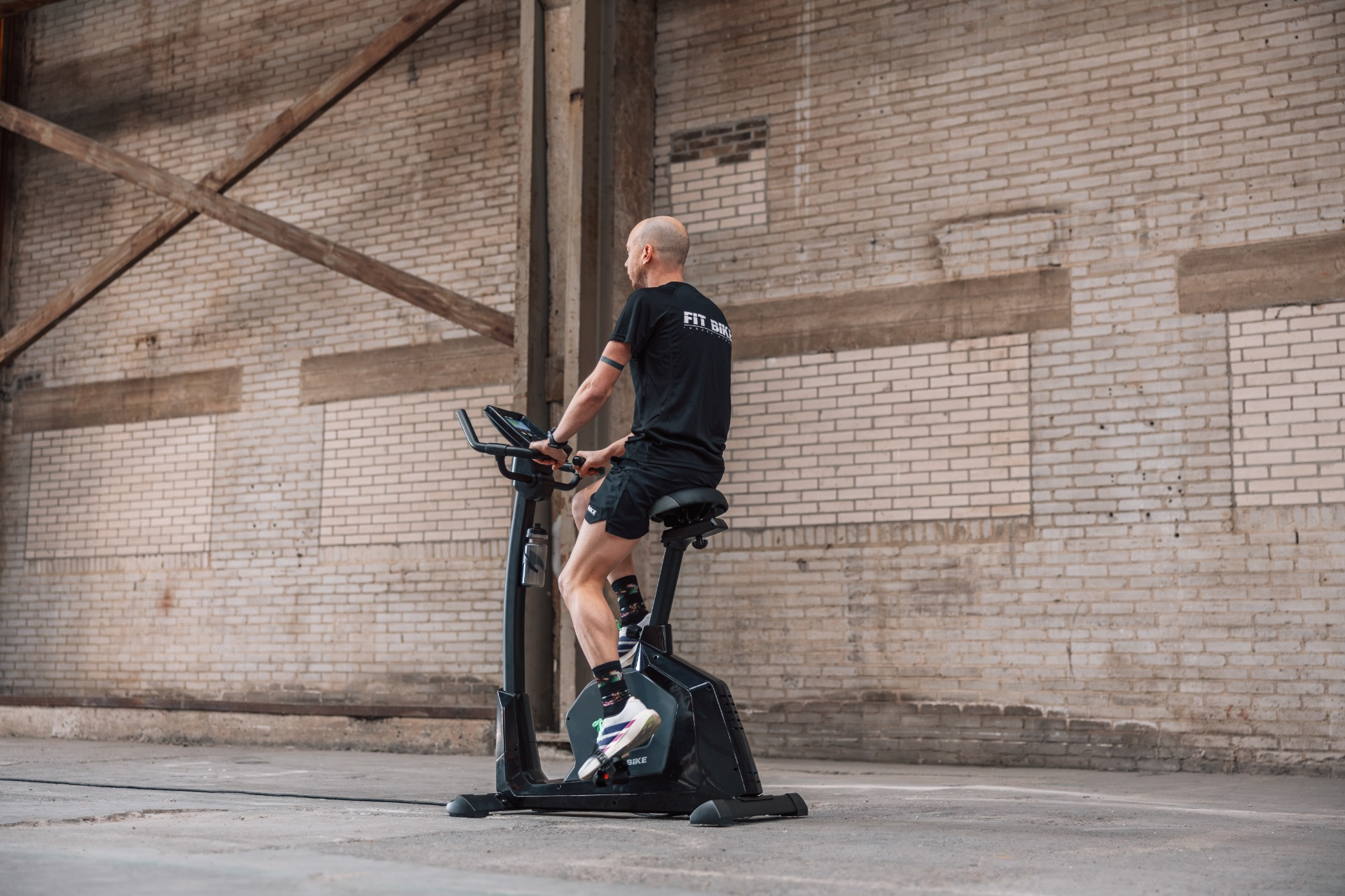 Un homme sur un vélo d'appartement devant un mur de briques.