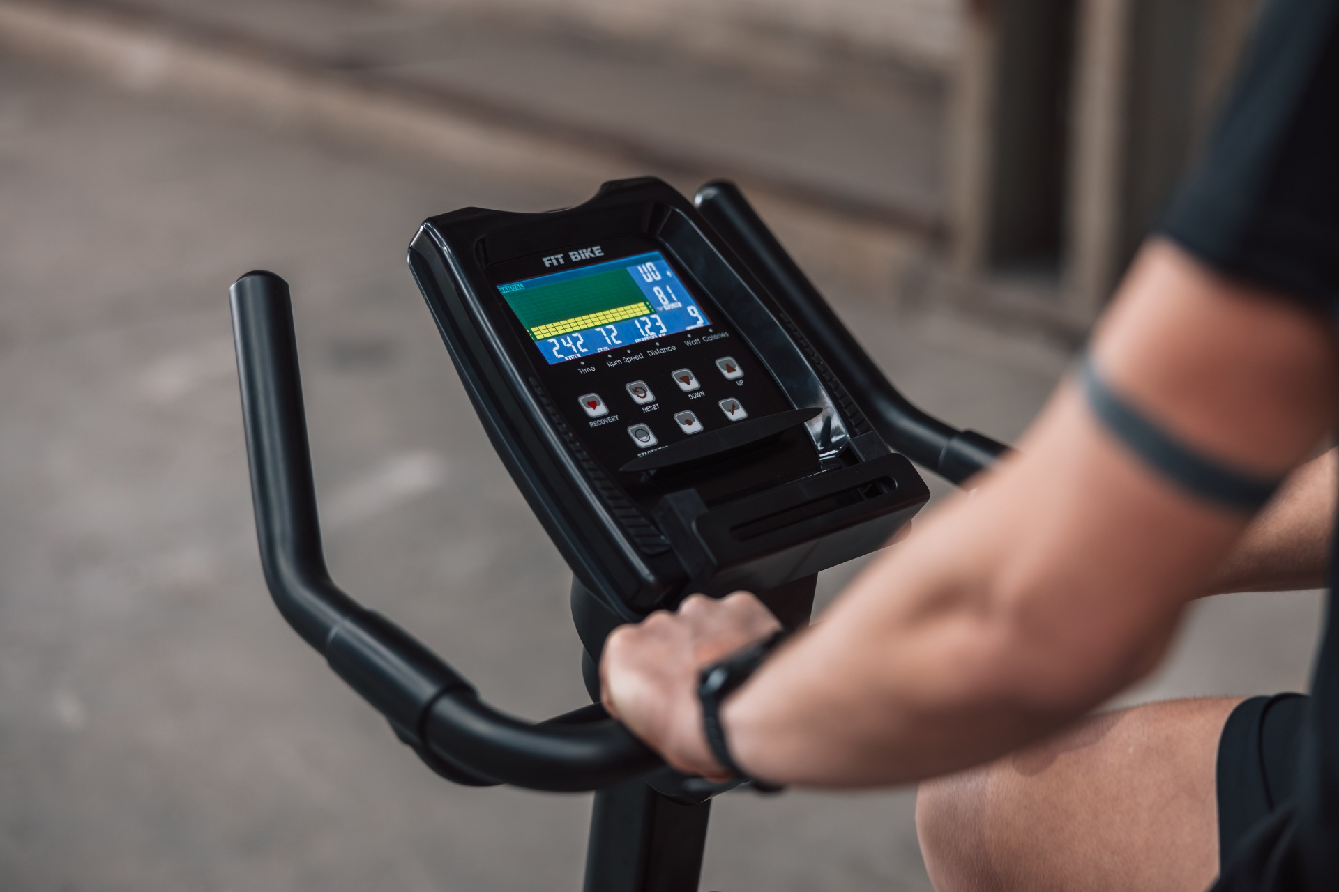 Gros plan de l'écran d'un vélo d'appartement avec un bras tenant le guidon.