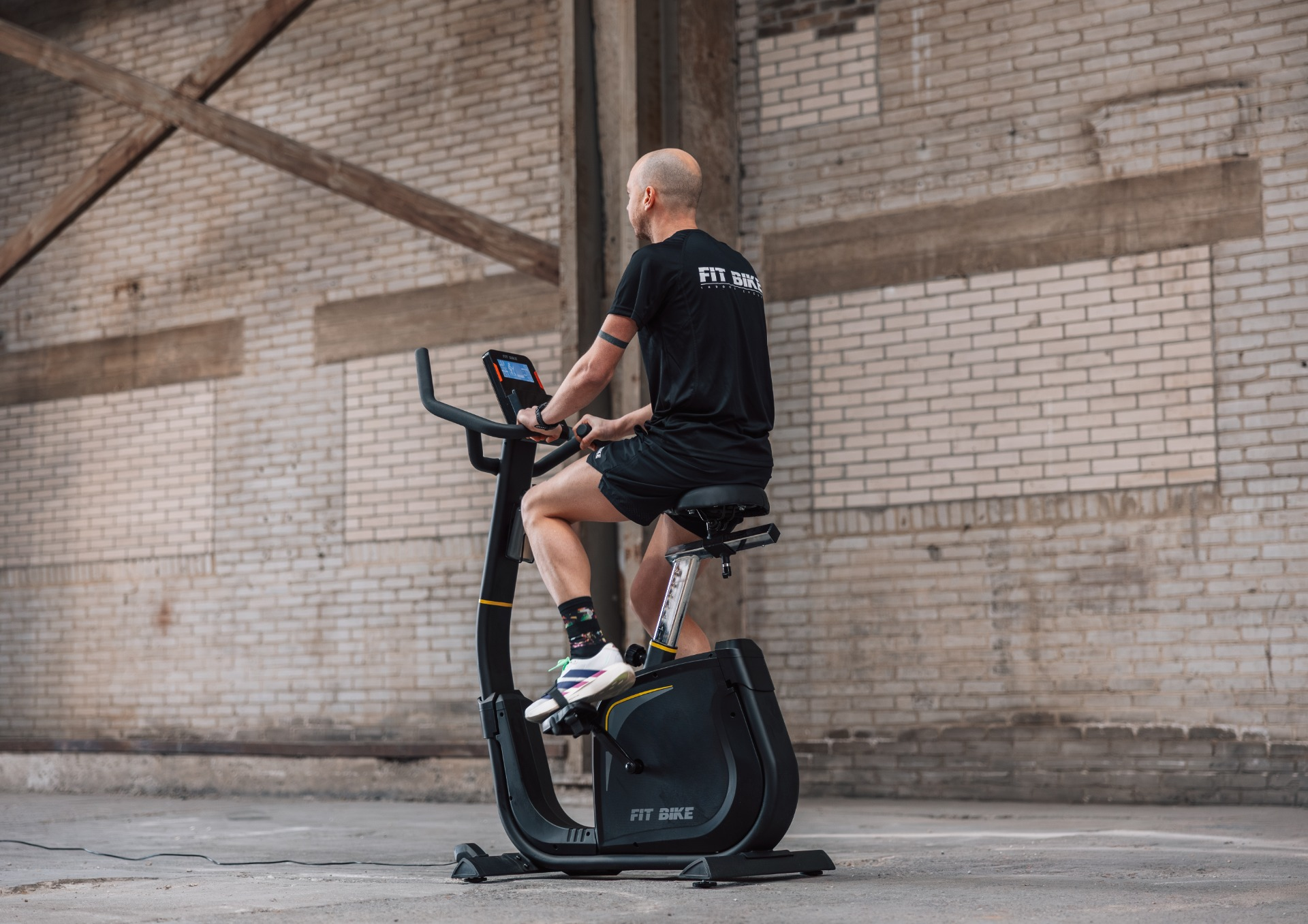 Un homme sur un vélo d'appartement noir devant un mur de briques.