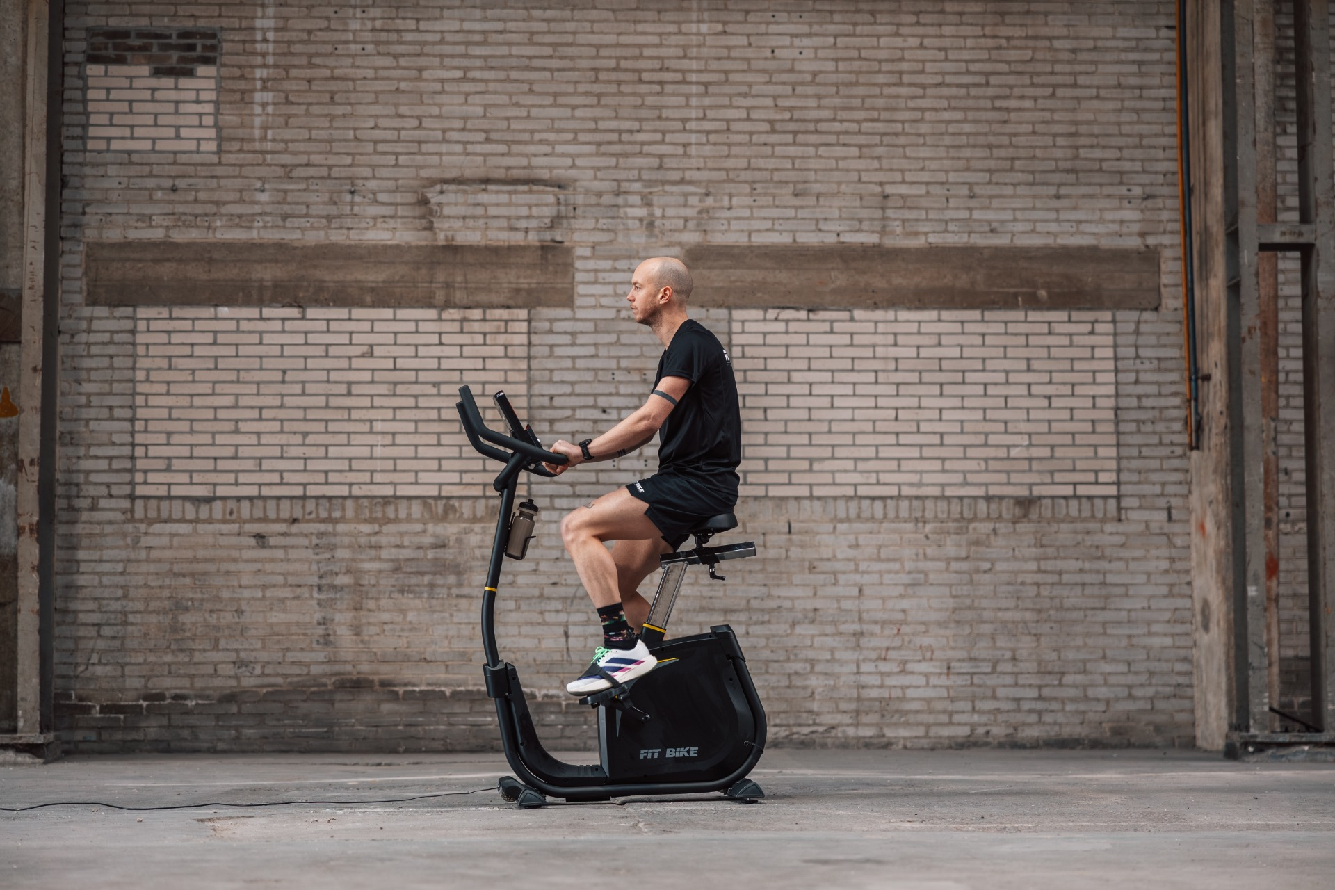 Homme sur un vélo d'appartement noir devant un mur de briques.