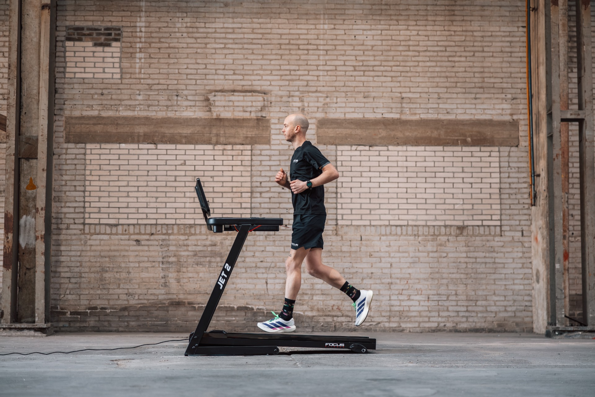 Homme courant sur tapis roulant dans un cadre industriel avec mur de briques.