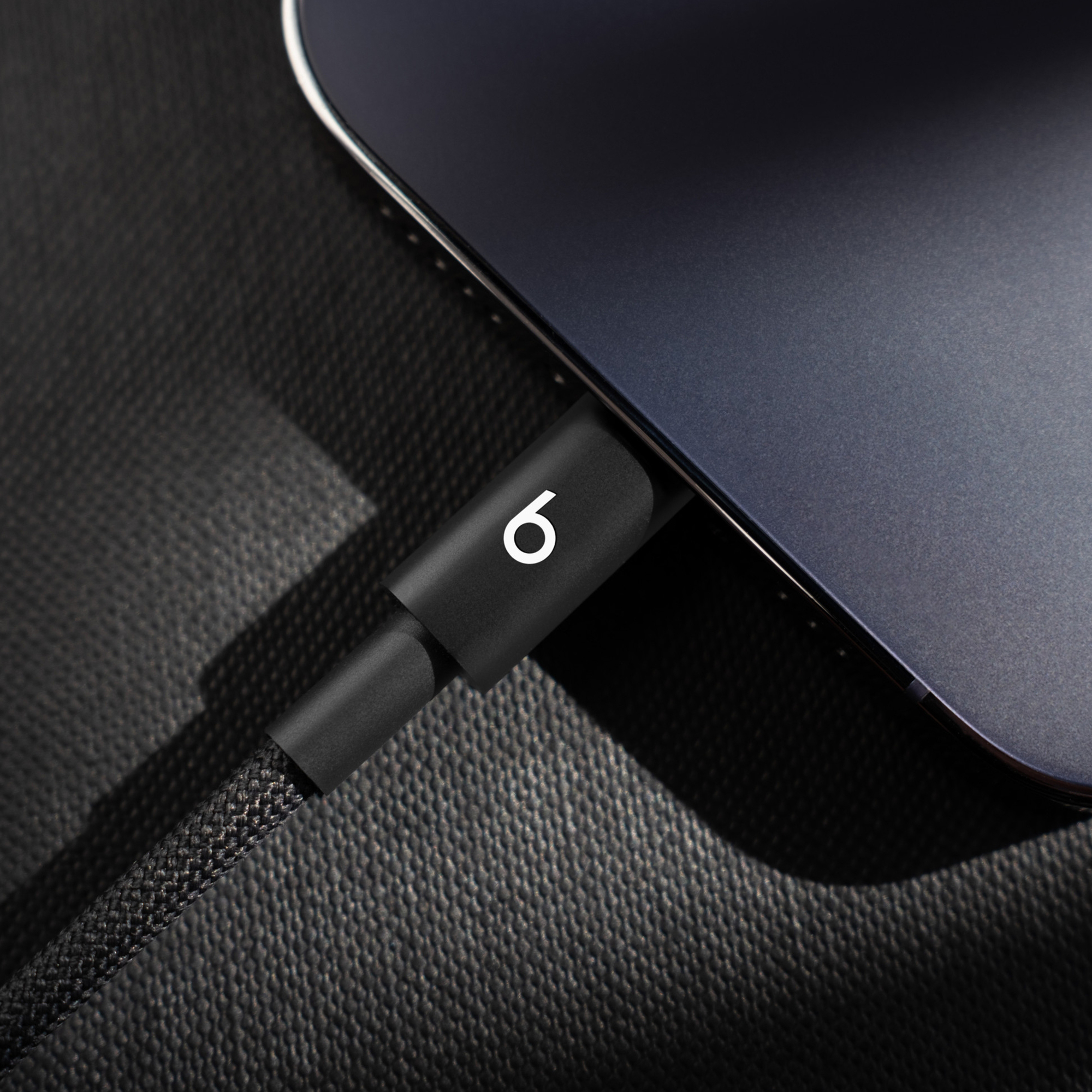 Czarny kabel ładujący z białym logo 'b' jest podłączony do ciemnego urządzenia.