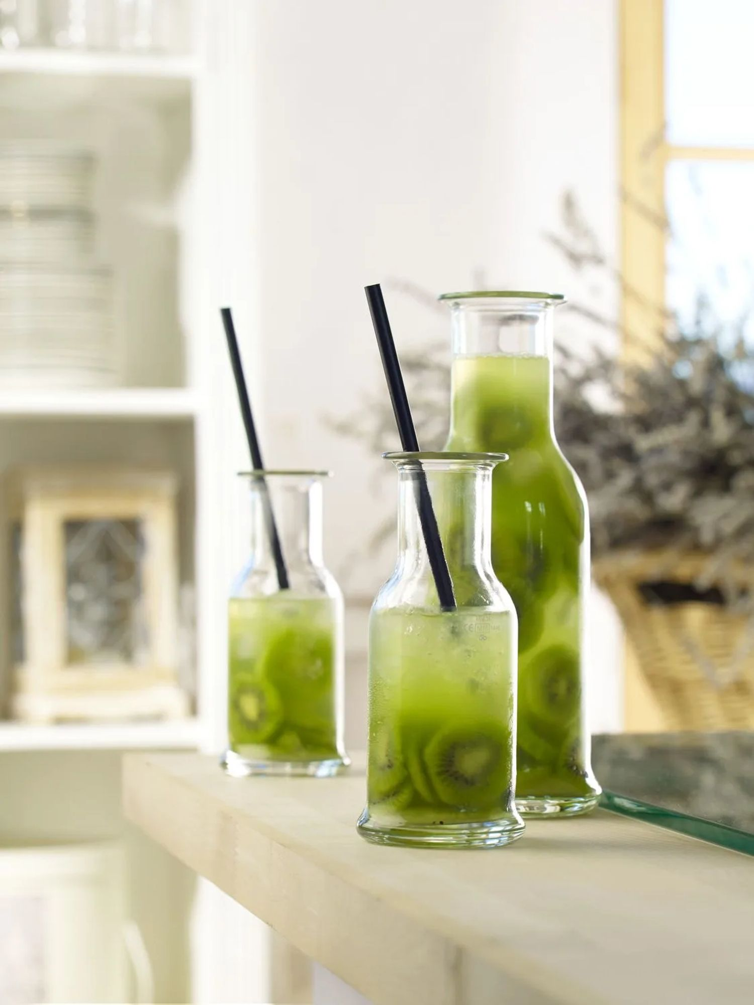 Three glass bottles with green drink and kiwi slices. Black straws.