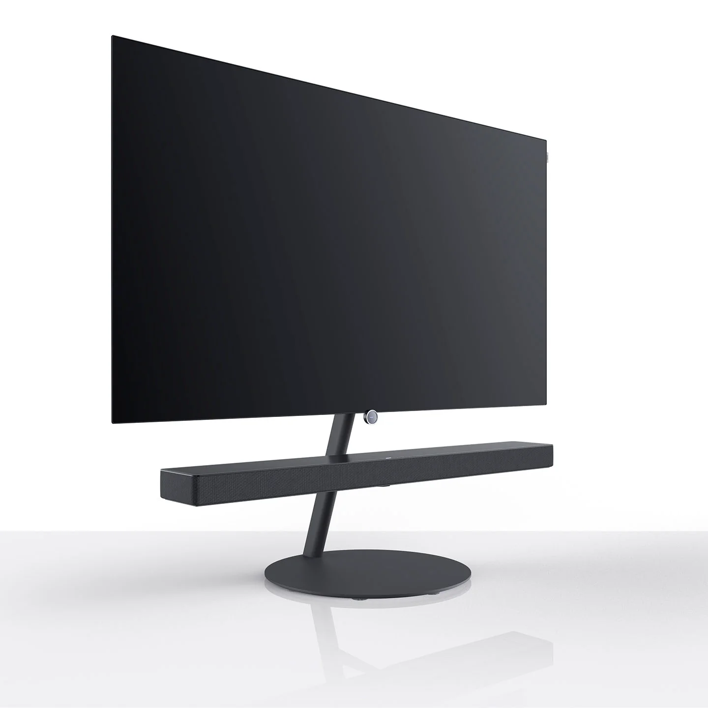 Yuvarlak stant üzerinde soundbar'lı siyah TV, beyaz arka plan.