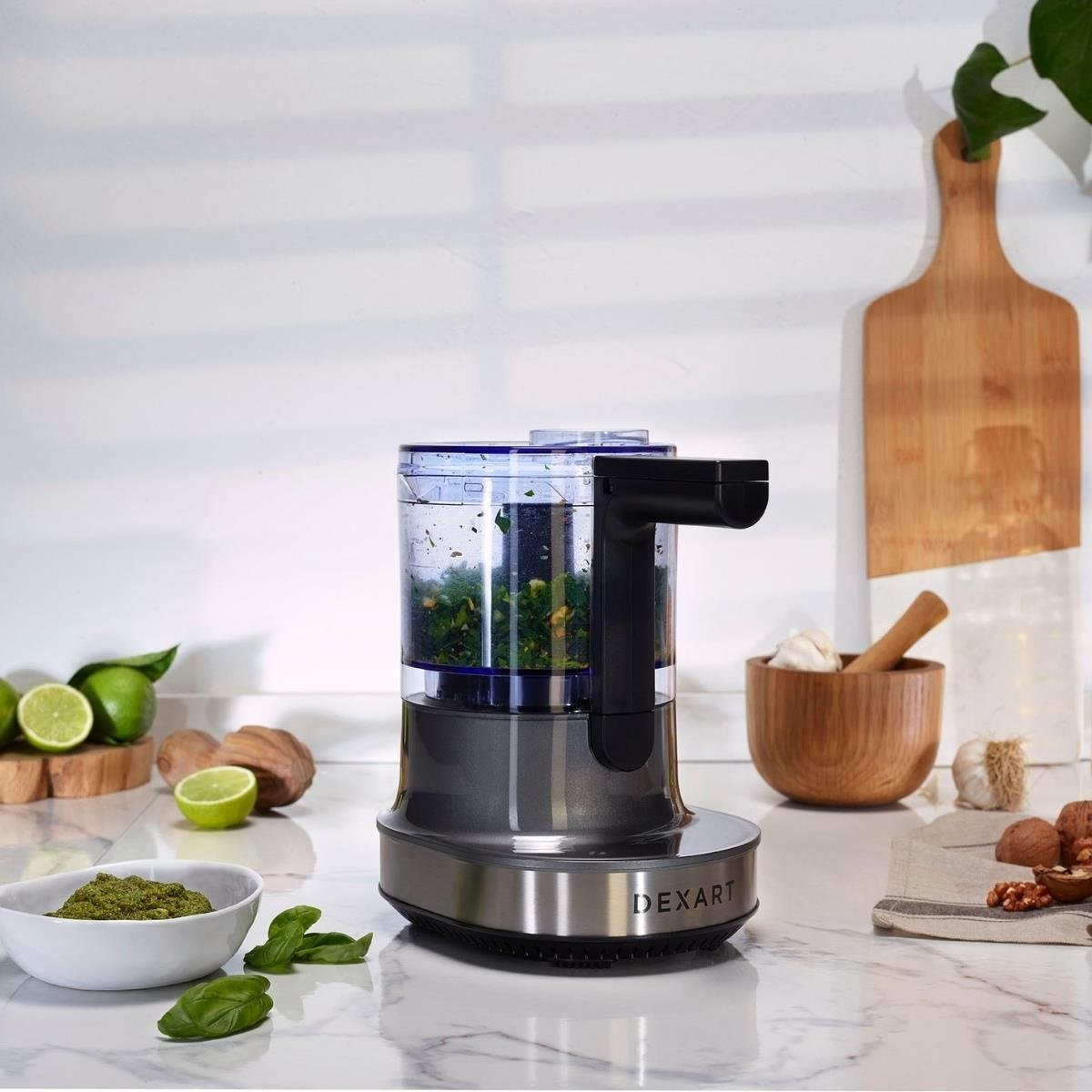 Doğranmış otlar içeren mutfak doğrayıcısı, yanında pesto kasesi, misket limonu ve ceviz.