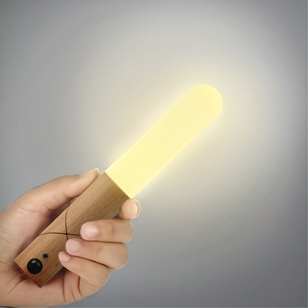 Una mano sostiene una lámpara de madera brillante que emite luz cálida.