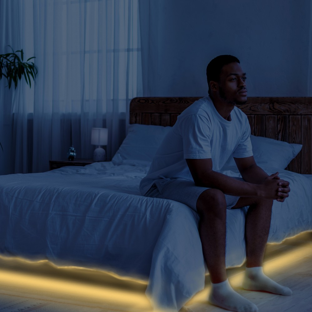 Hombre sentado en una cama a oscuras, mirando pensativo a un lado.