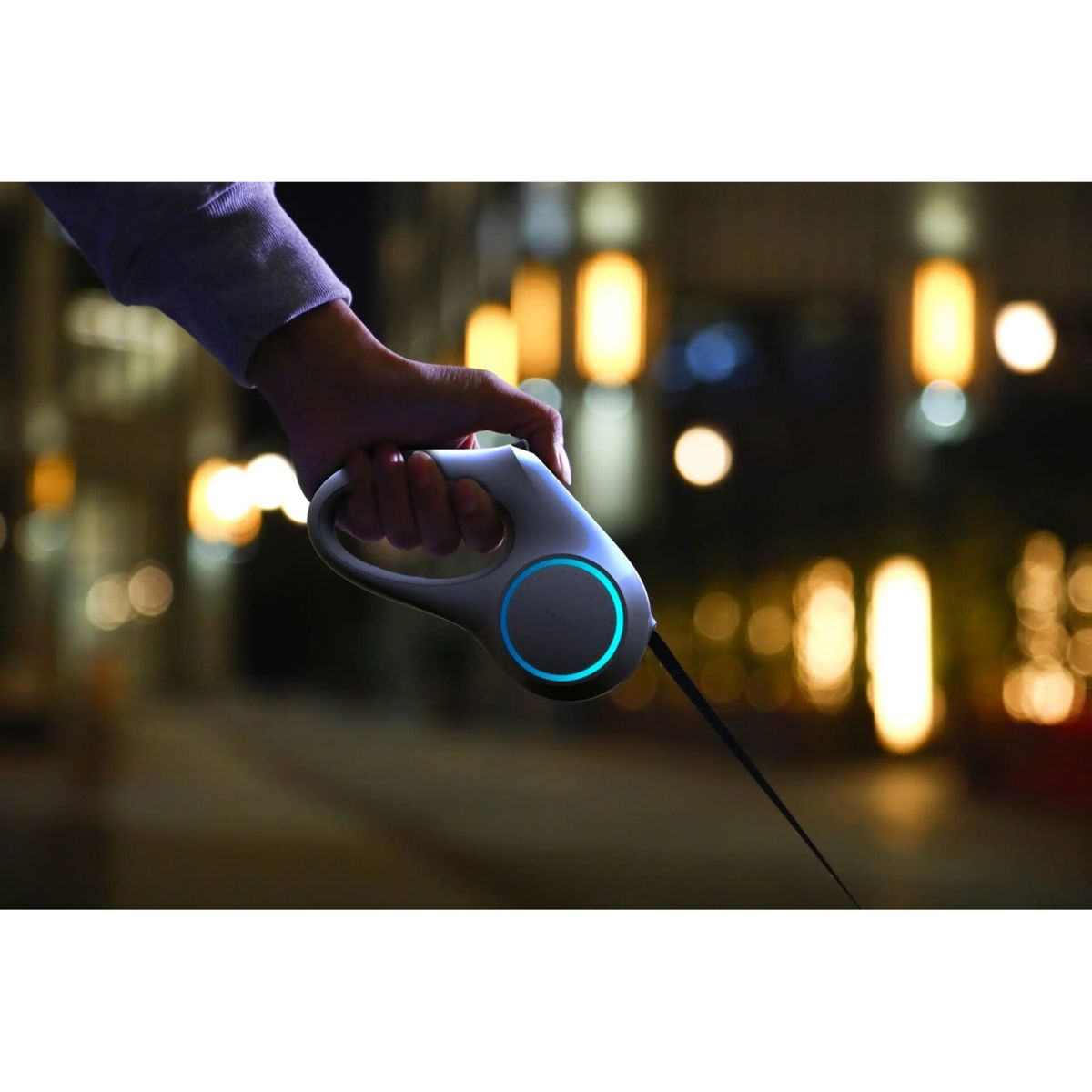 Mano sujetando correa de perro con anillo de luz azul por la noche.