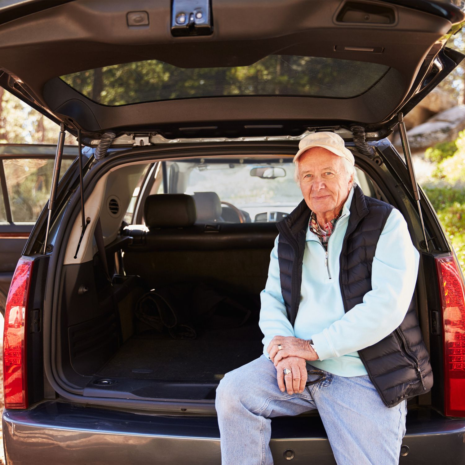 Un anciano se sienta en el maletero abierto de un coche al aire libre.