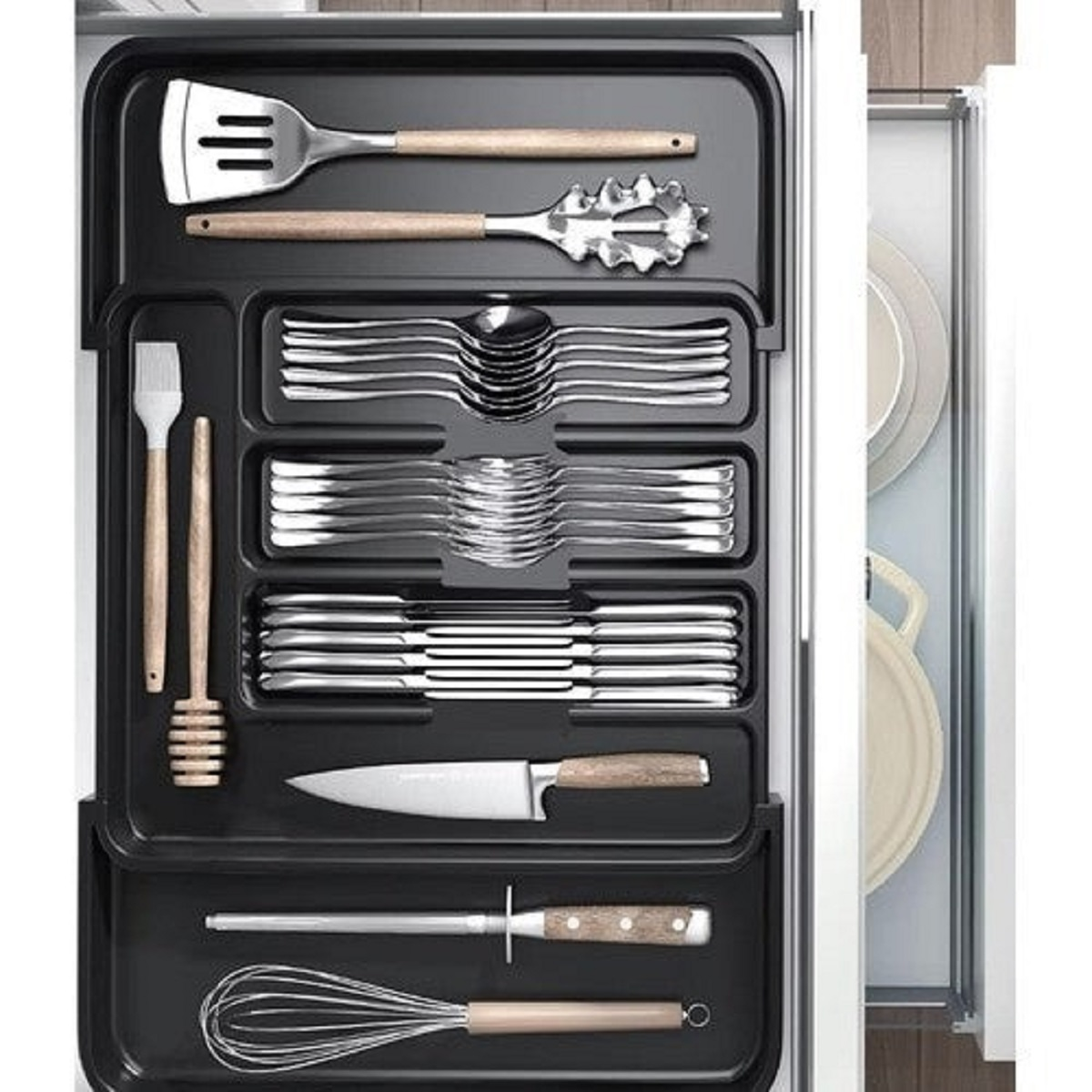 Utensilios de cocina en un organizador: espátula, cuchara para pasta, cubiertos, cuchillo, chaira, batidor.