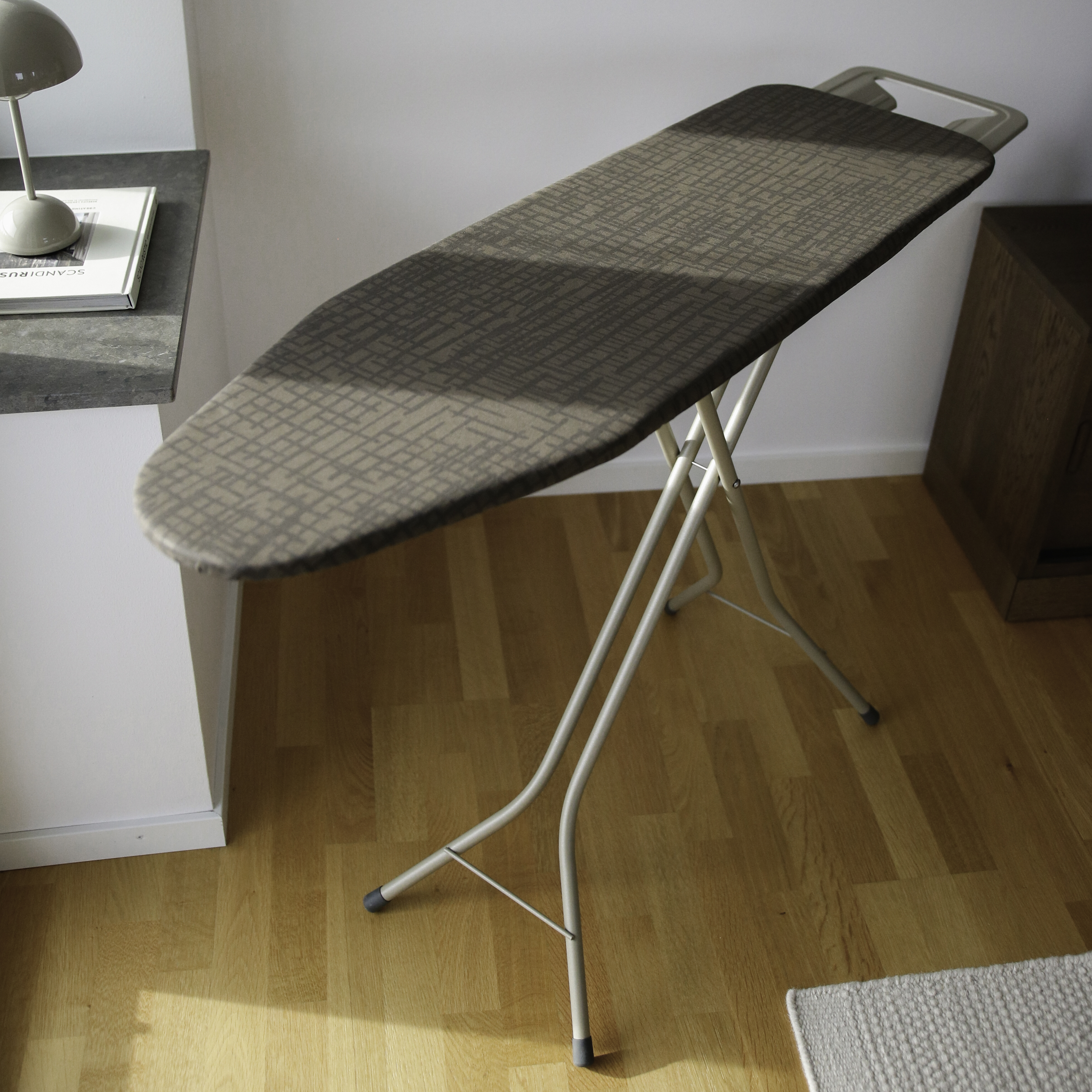 Une planche à repasser avec une housse à motifs est sur un parquet.