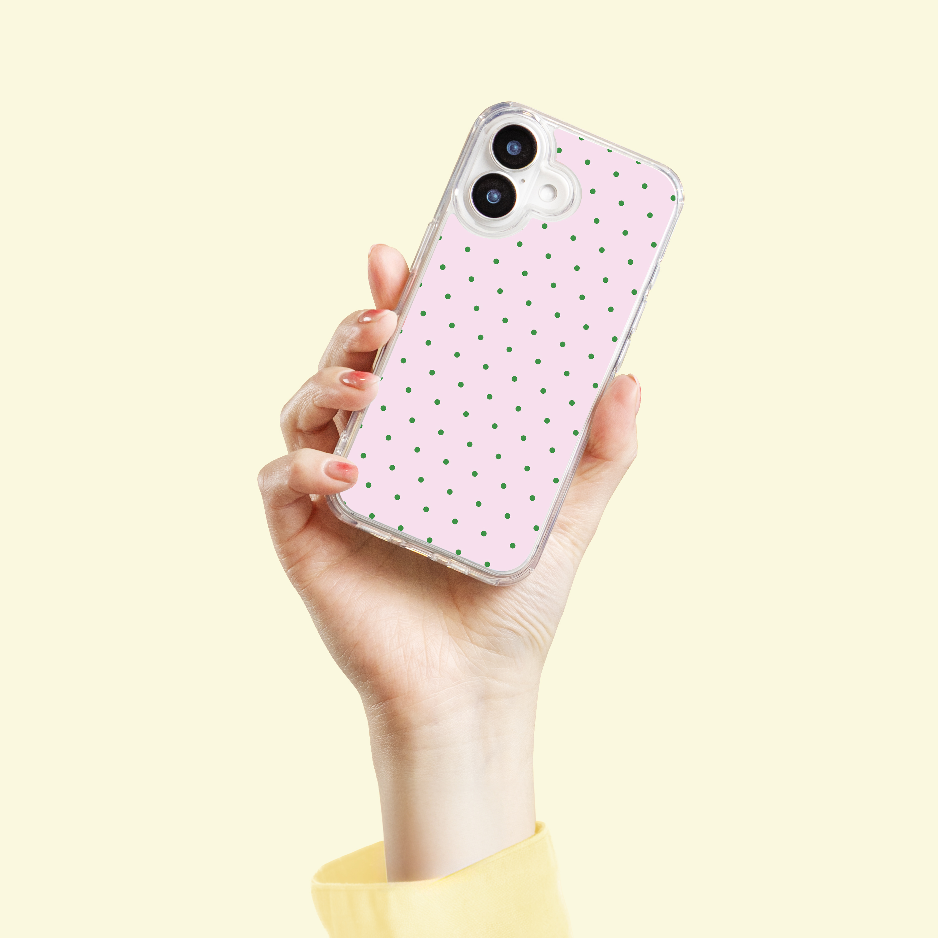 Een hand houdt een telefoon vast met een roze achtergrond met groene stippen.