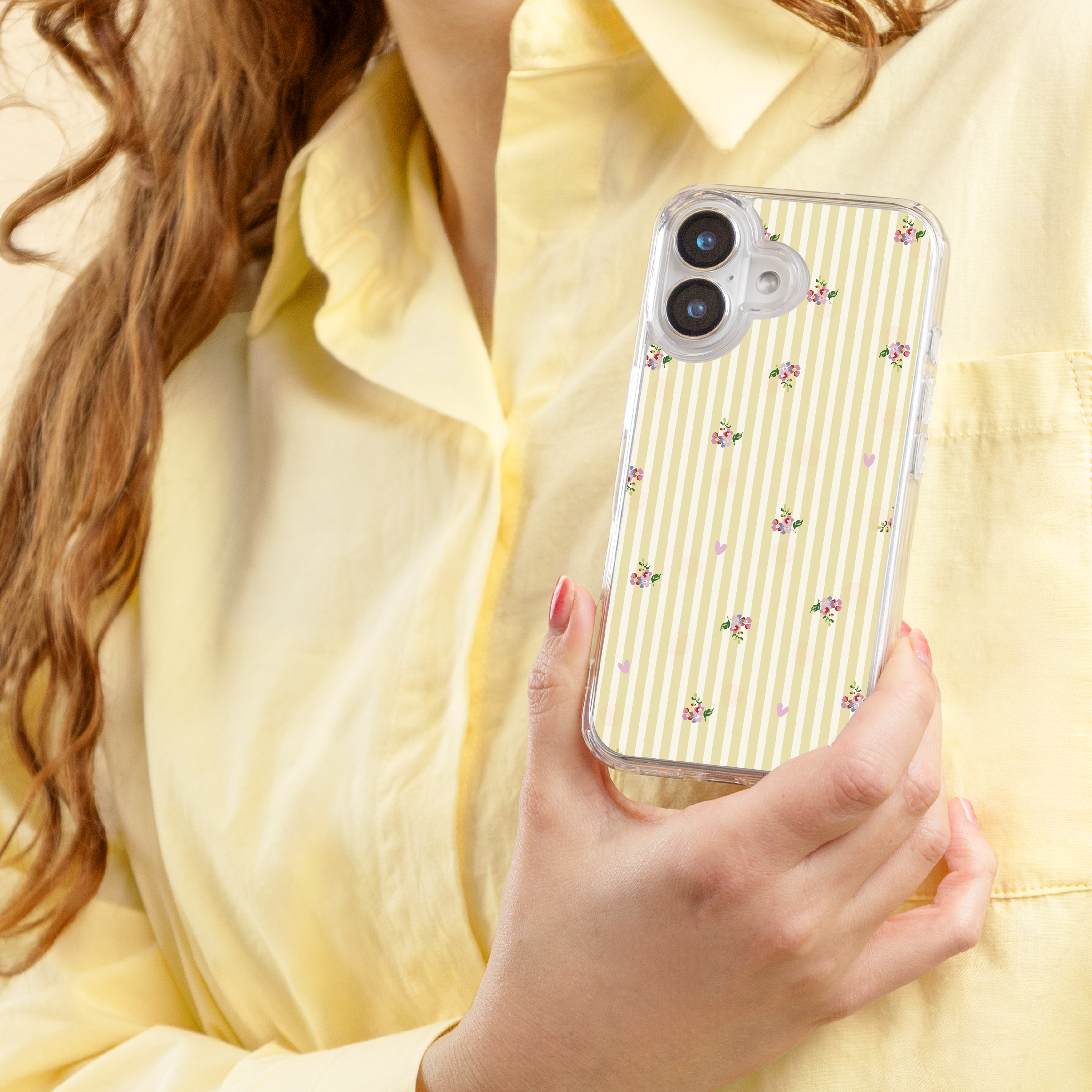 Een persoon in een geel shirt houdt een doorzichtige telefoon met bloemenpatroon vast.